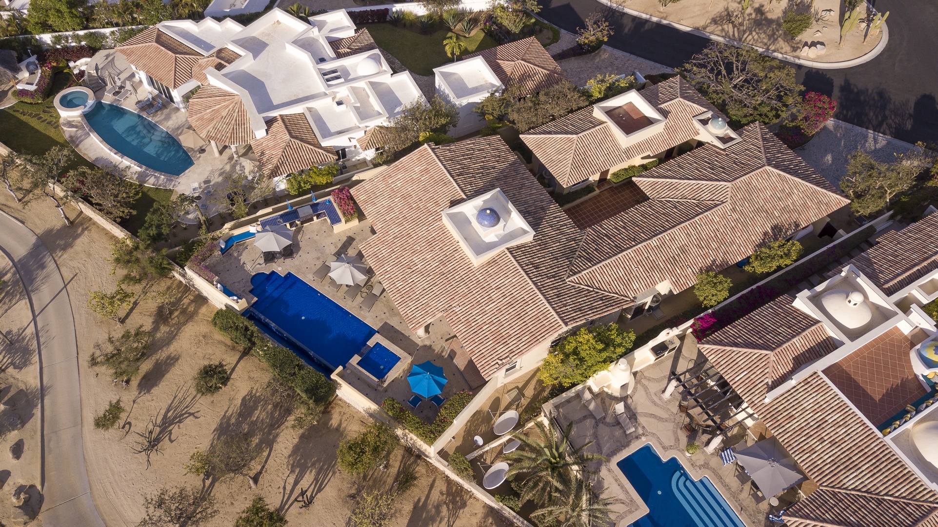 Aerial view of an upscale residential development featuring Mediterranean-style villas with tile roofs and private swimming pools.