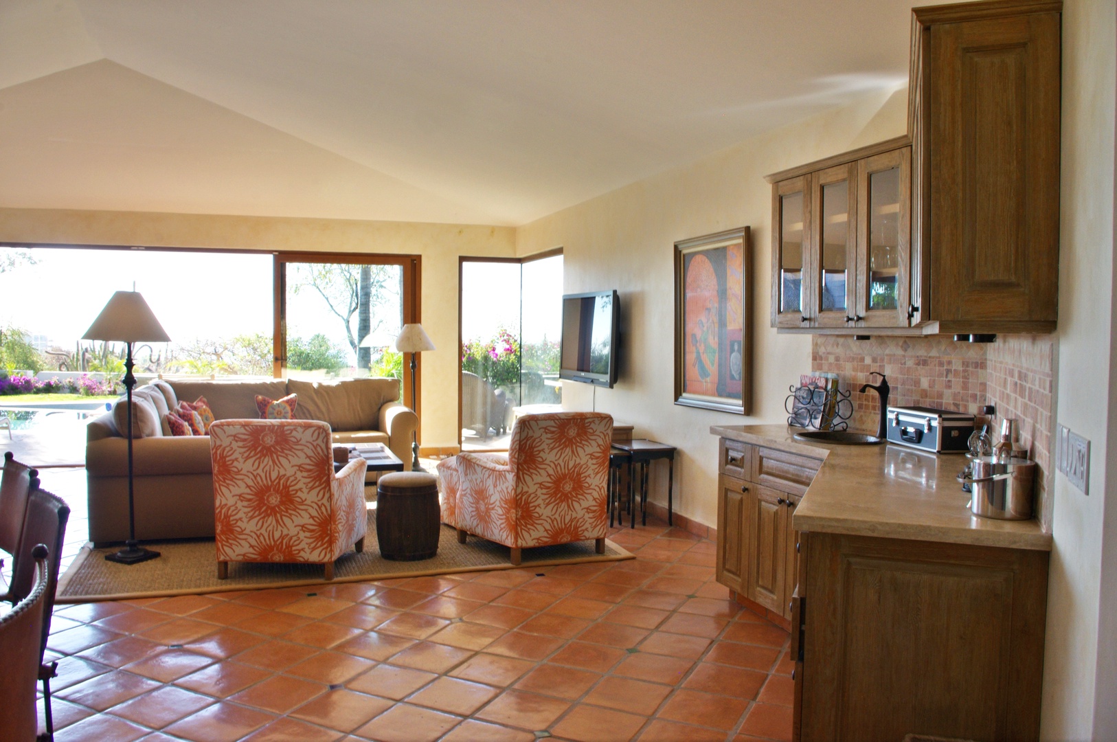 Your spacious open-concept living area flows seamlessly from the cozy lounge to the full kitchen, with terracotta floors and large windows framing garden views.