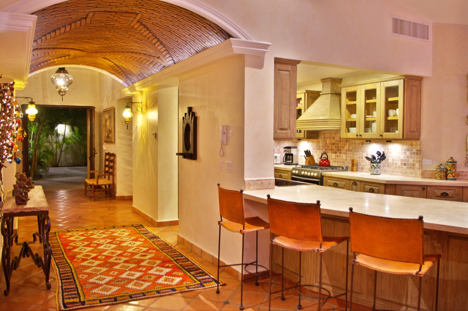 Step into a beautifully designed kitchen with warm wooden cabinetry, a spacious island with leather seating, and charming archways that invite you to explore your vacation home.
