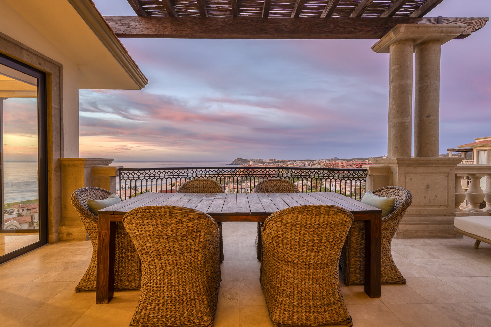 A spacious terrace framing stunning coastal views and soft sunset hues, with elegant woven seating surrounding a handsome wooden dining table. Your perfect perch for savoring morning coffee or twilight relaxation.