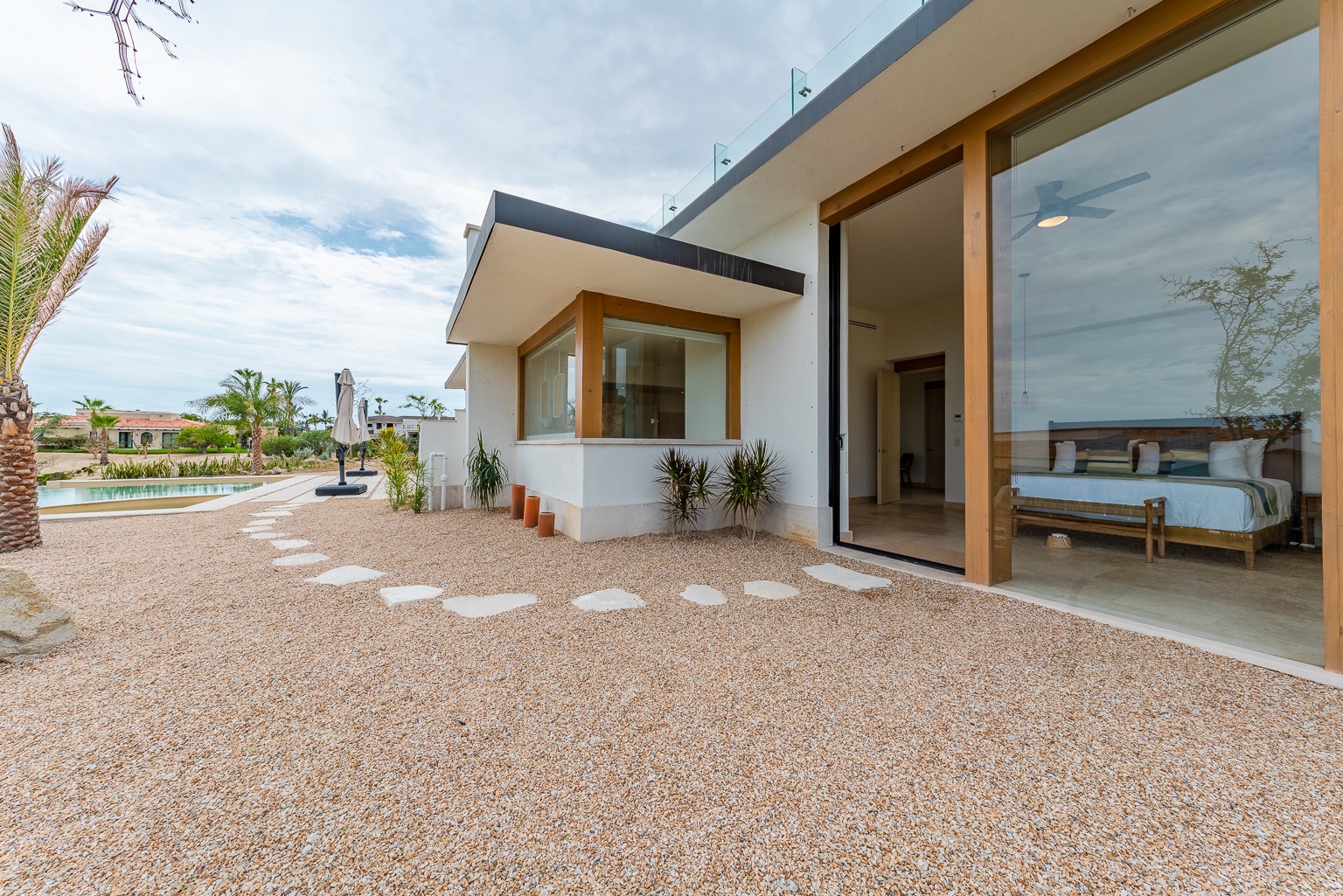 This modern villa showcases clean architectural lines and a sleek desert patio area with easy access to the bedroom suite, surrounded by tropical landscaping and peaceful neighborhood views.