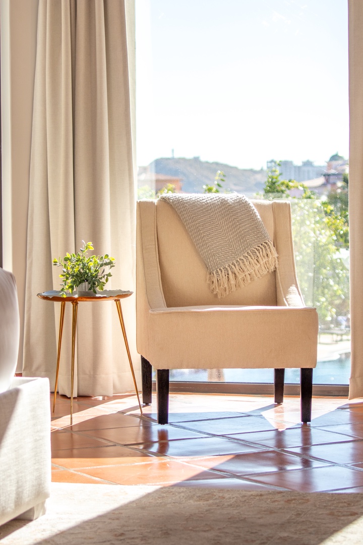 Settle into your cozy reading chair by the sunny window, where soft natural light and a gentle throw invite you to unwind and soak in peaceful moments.