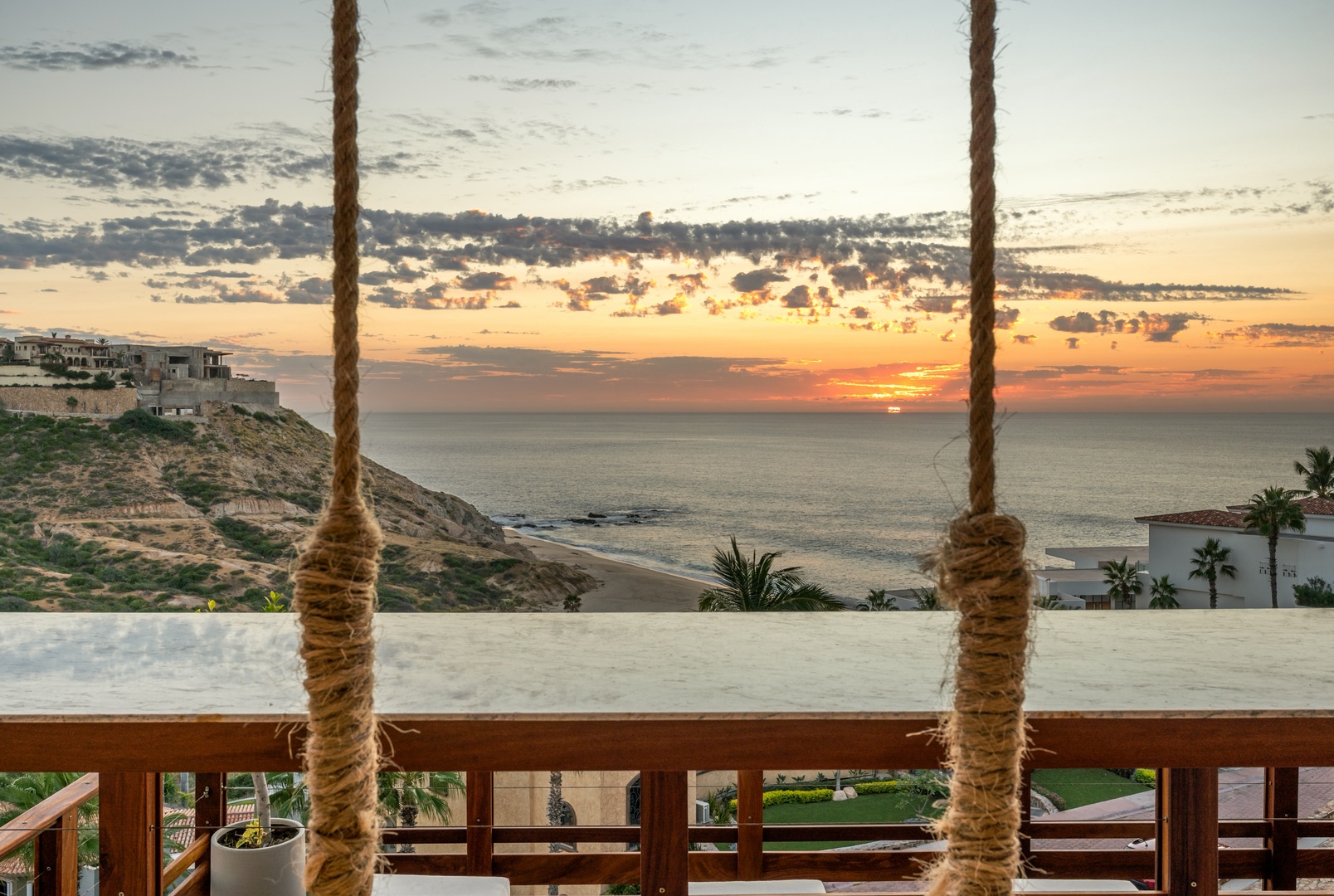 Stunning coastal sunset views over the ocean with palm trees and hillside properties visible nearby. The property's elevated position offers expansive vistas of the surrounding area.