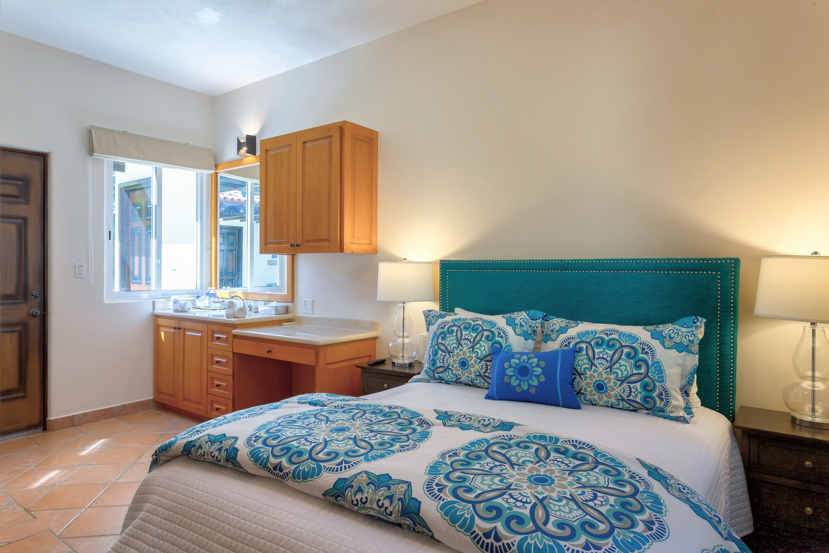 Relax in your bright bedroom with vibrant blue linens, built-in workspace, and peaceful street views through large windows.