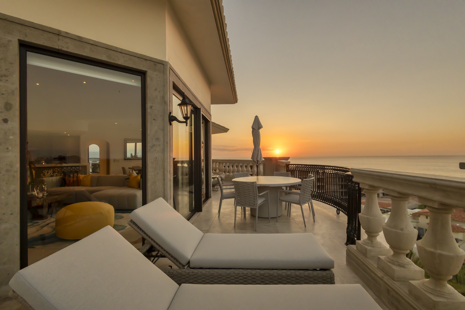 This beachfront terrace offers stunning sunset views over calm waters, featuring comfortable loungers, outdoor dining, and direct access to the interior living space—ideal for relaxing evenings by the sea.