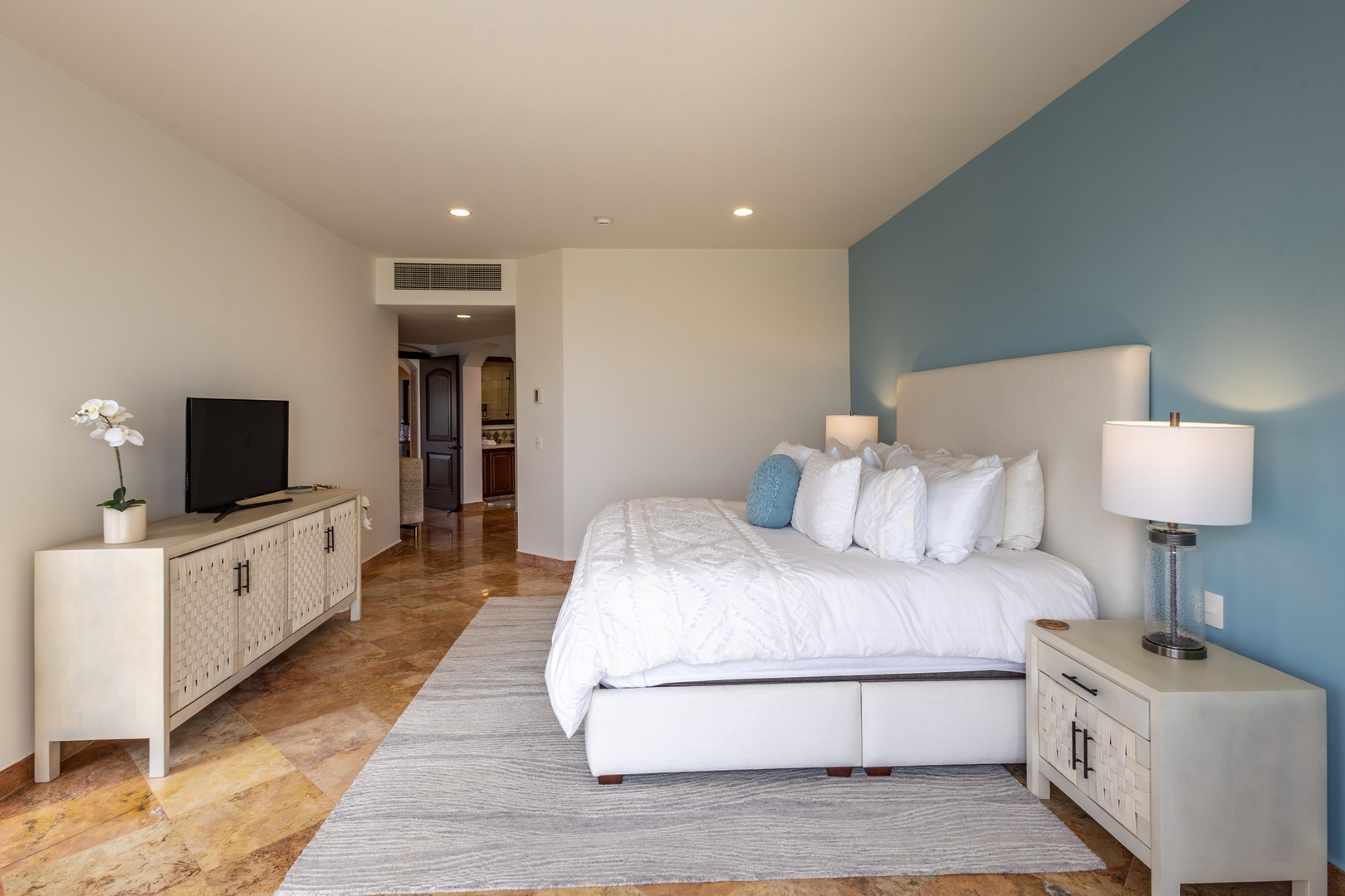 Sink into plush white linens and let the calming blue accent wall wash away your stress in this serene bedroom sanctuary.
