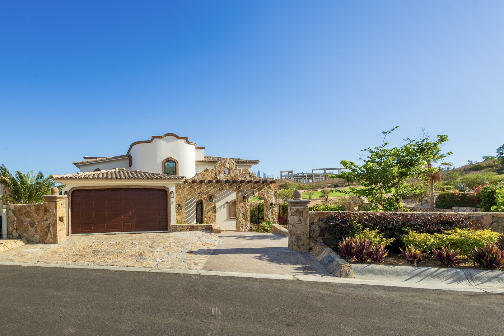 Mediterranean-style villa with stone accents and garage, framed by lush landscaping and hillside views under clear blue skies.