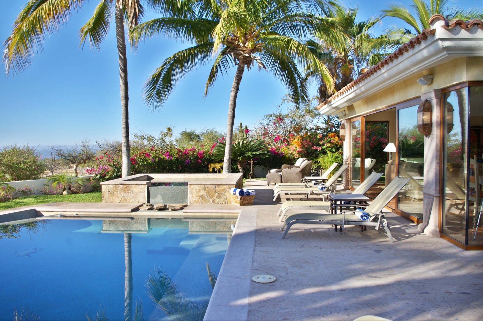 Lounge poolside under swaying palms, surrounded by vibrant tropical blooms. Your private oasis awaits, where sun-kissed days blend seamlessly with relaxation and scenic mountain views.