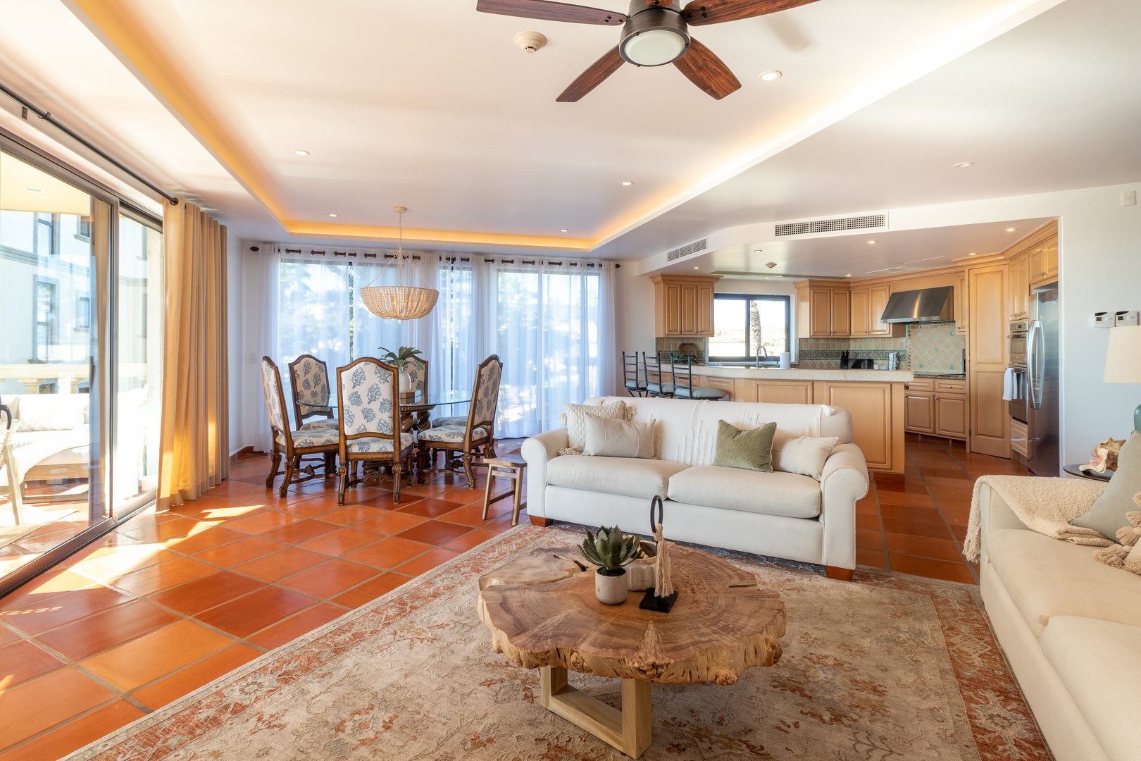 Sink into plush sofas and gather around the rustic live-edge coffee table in your open-concept living space, where natural light pours through floor-to-ceiling windows and elegant terracotta tiles add warmth underfoot.