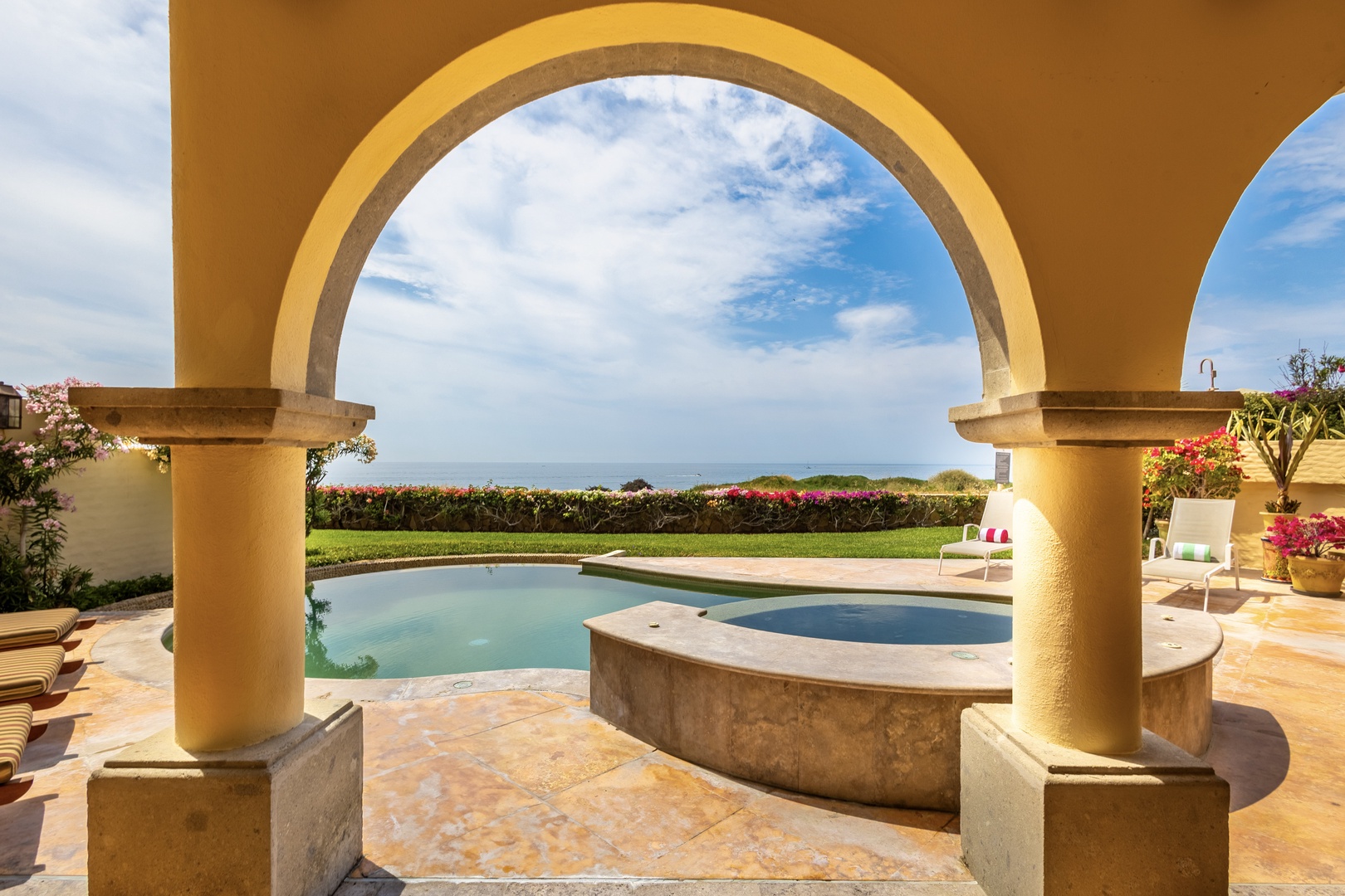 Mediterranean-style archway frames a sparkling pool, lush gardens, and tranquil ocean horizon—a stunning coastal escape where relaxation awaits at every turn.