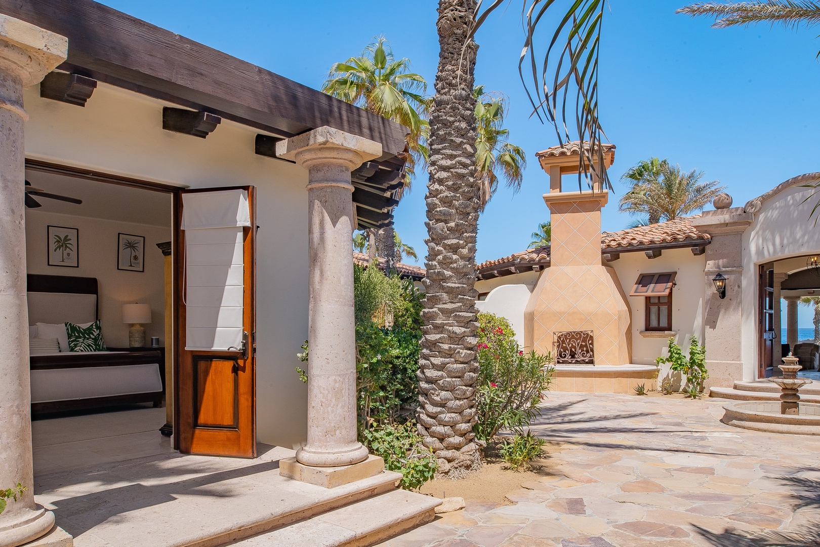 Elegant villa courtyard featuring stone columns, palm trees, and an outdoor fireplace creates a peaceful Mediterranean-style retreat.