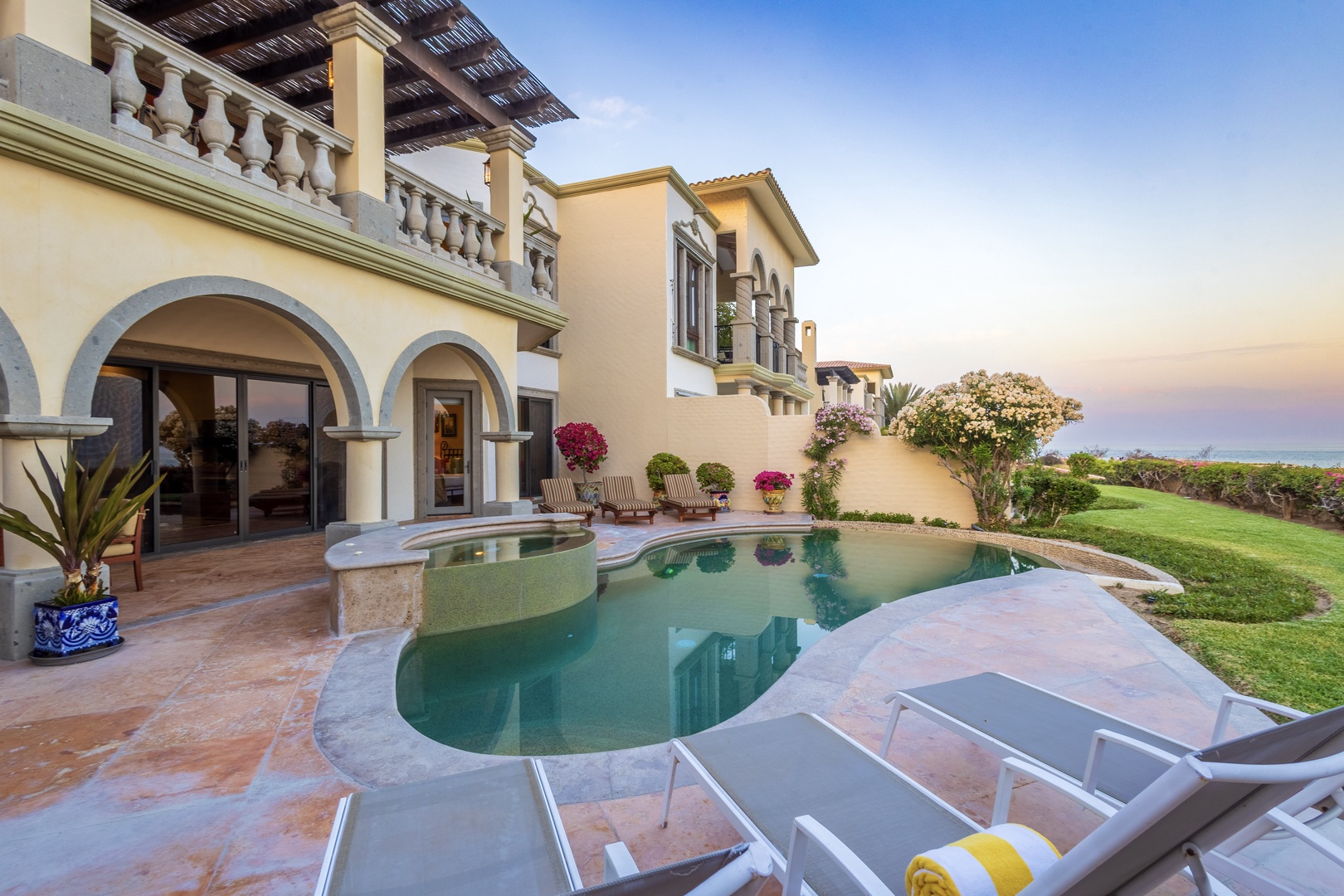 A private pool nestled beside elegant archways, lush gardens, and golden-hour skies creates a serene coastal escape where relaxation meets timeless design.