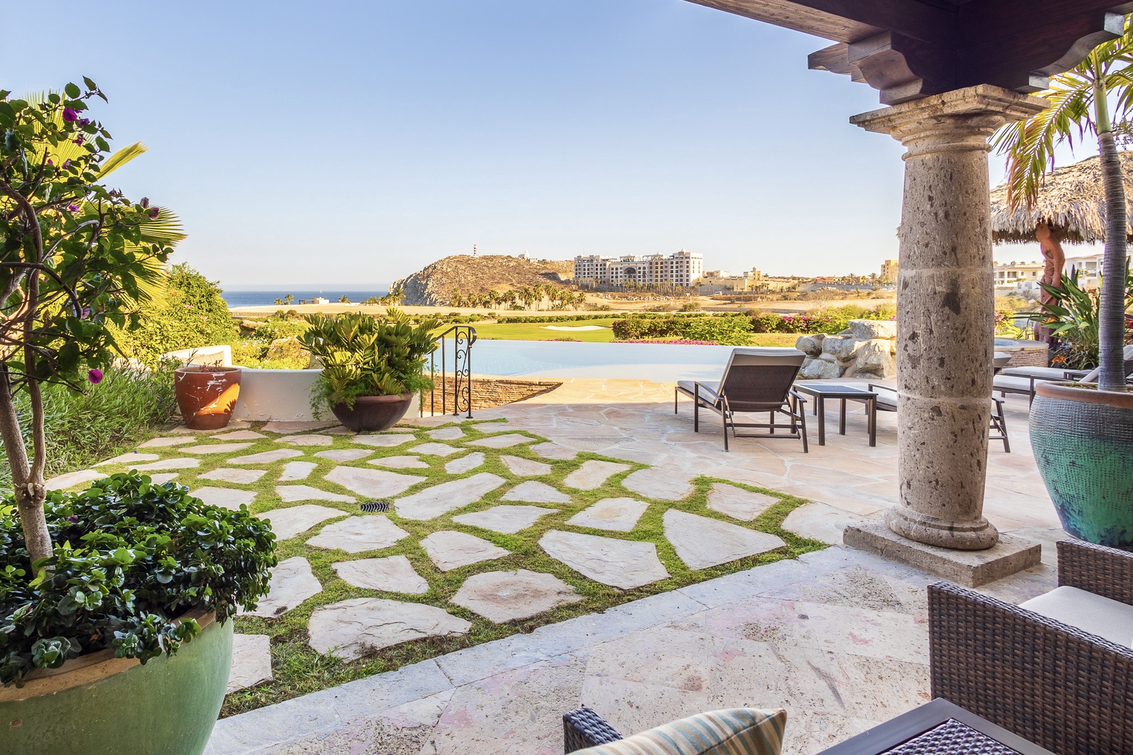 Private terrace with coastal resort views, lush greenery, and elegant stone columns overlooking tranquil lagoon and seaside landscape beyond.