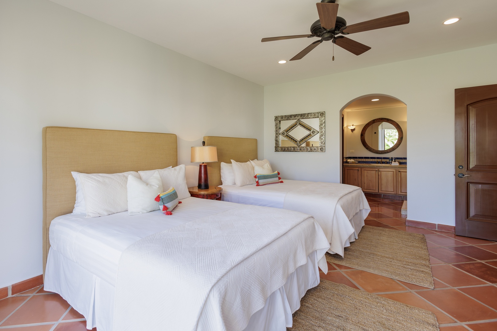 Sink into plush linens and unwind in your tranquil retreat featuring two queen beds, charming terracotta floors, and an en-suite bathroom framed by an elegant archway.