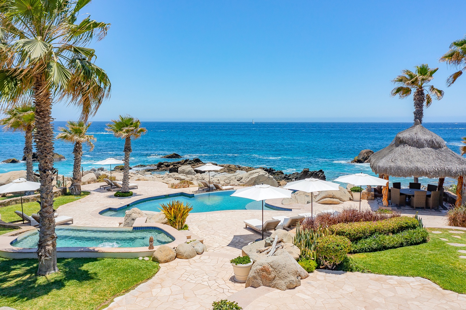 Oceanfront paradise with pristine pools, tropical palms, and endless azure waters stretching to the horizon.