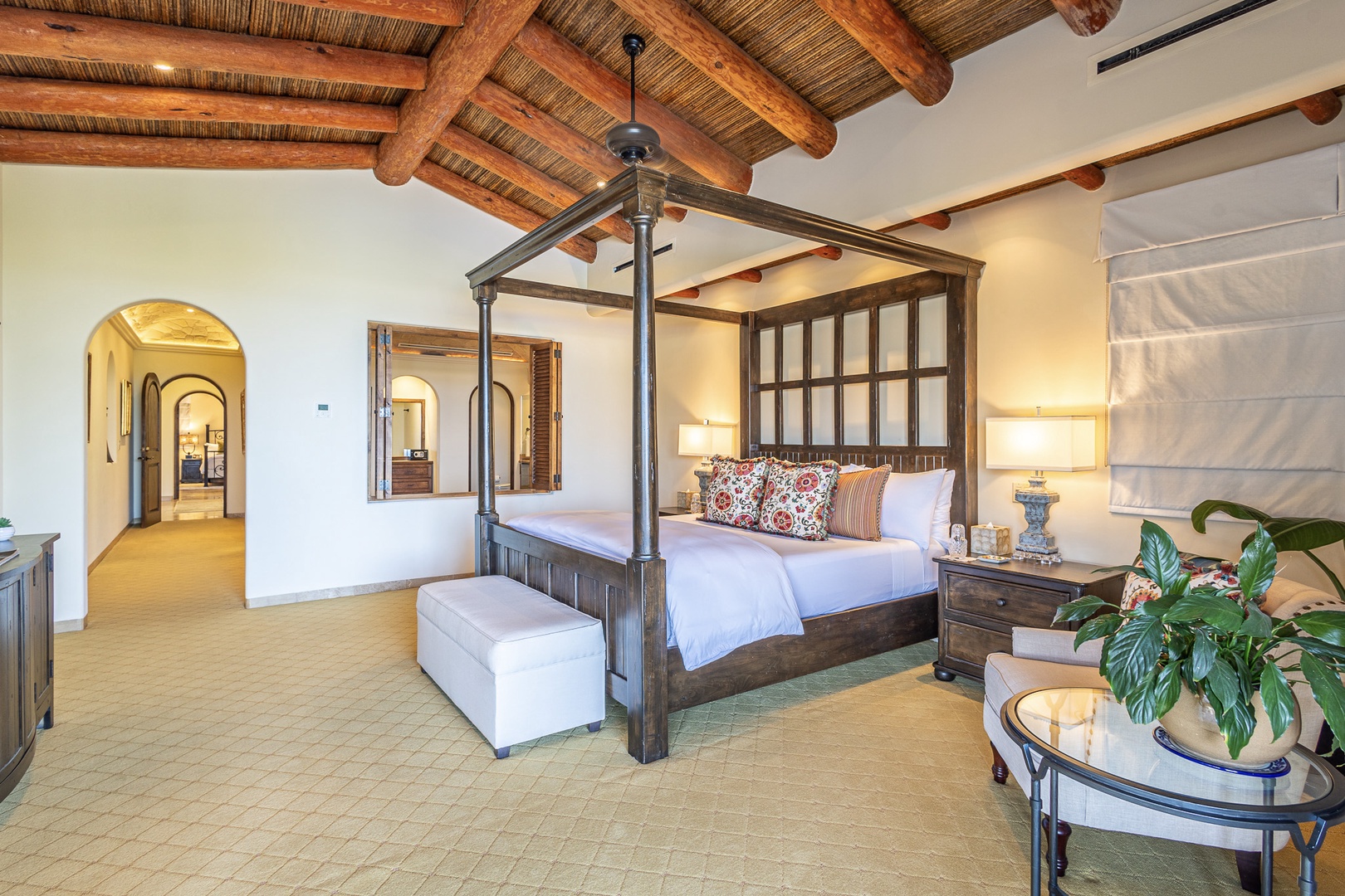 Unwind in your spacious retreat with a stunning canopy bed, rustic beamed ceilings, and serene arched details inviting peaceful rest.