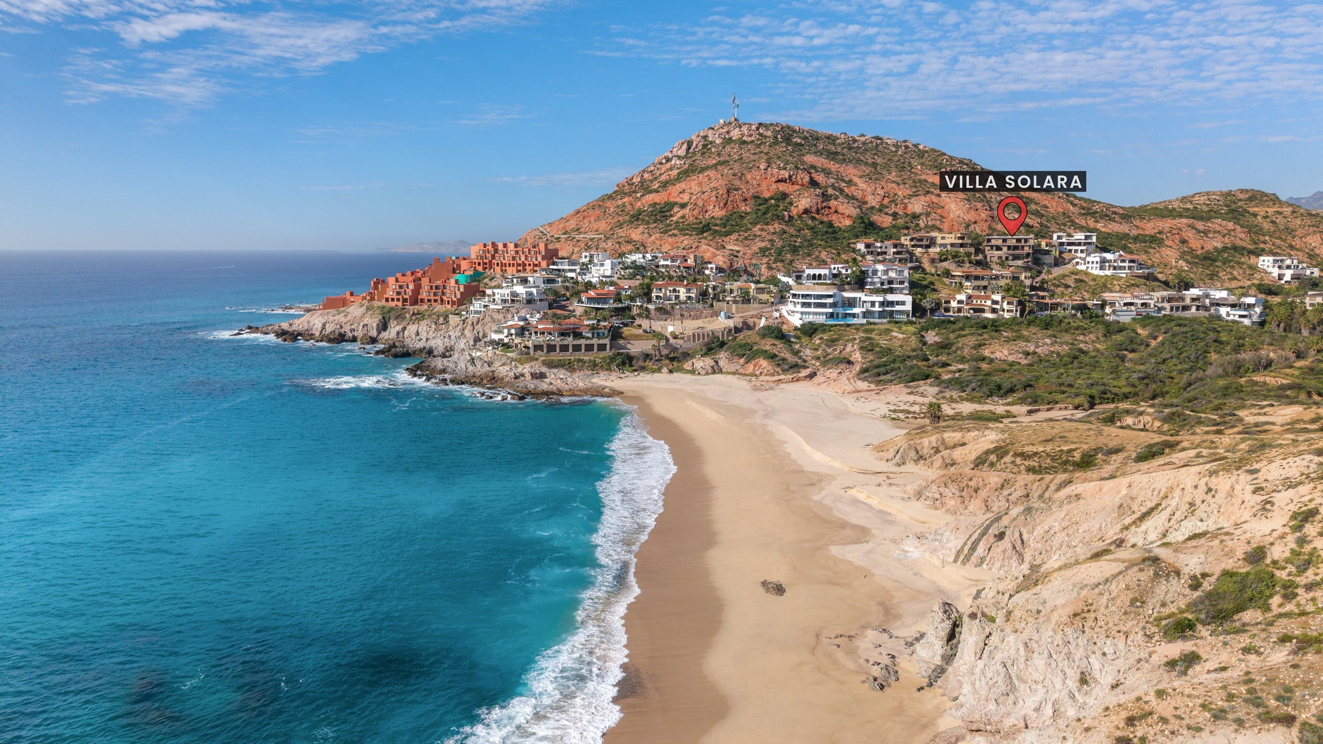 Coastal property perched above pristine beach and turquoise waters, surrounded by dramatic hills and scenic shoreline, offering a serene hillside escape.