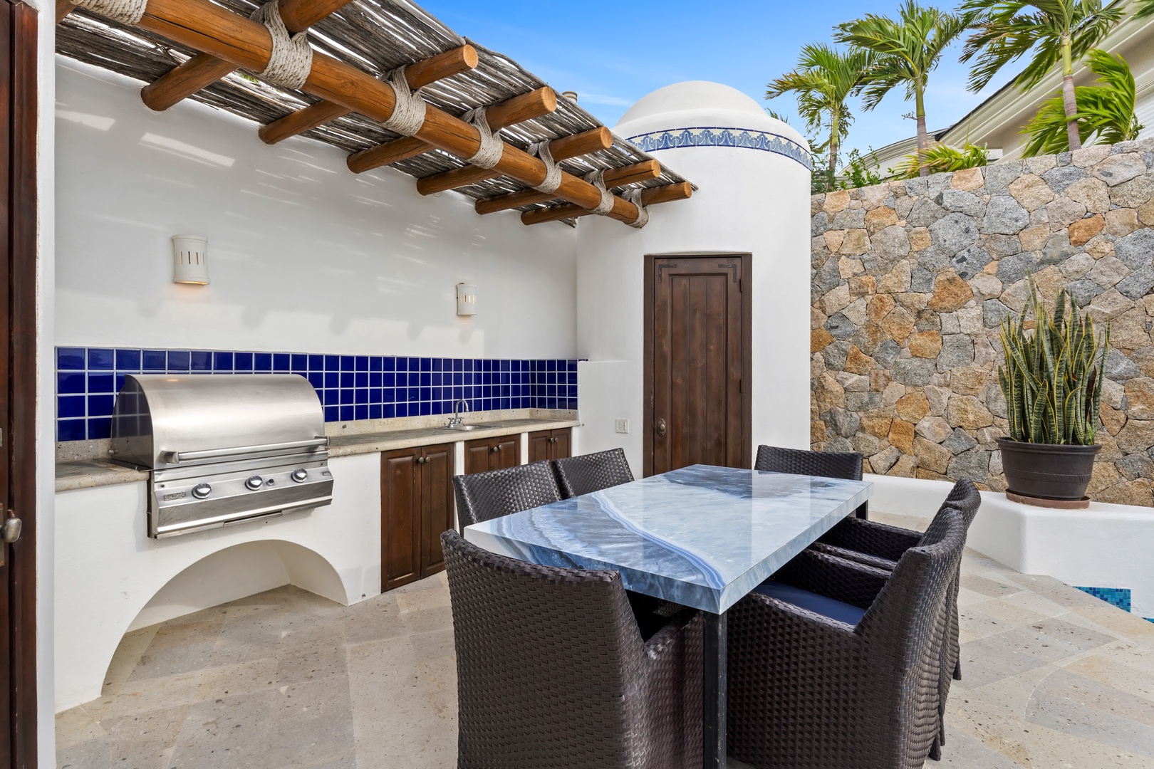 Your private outdoor kitchen awaits with marble dining table and professional grill under a traditional palapa roof.
