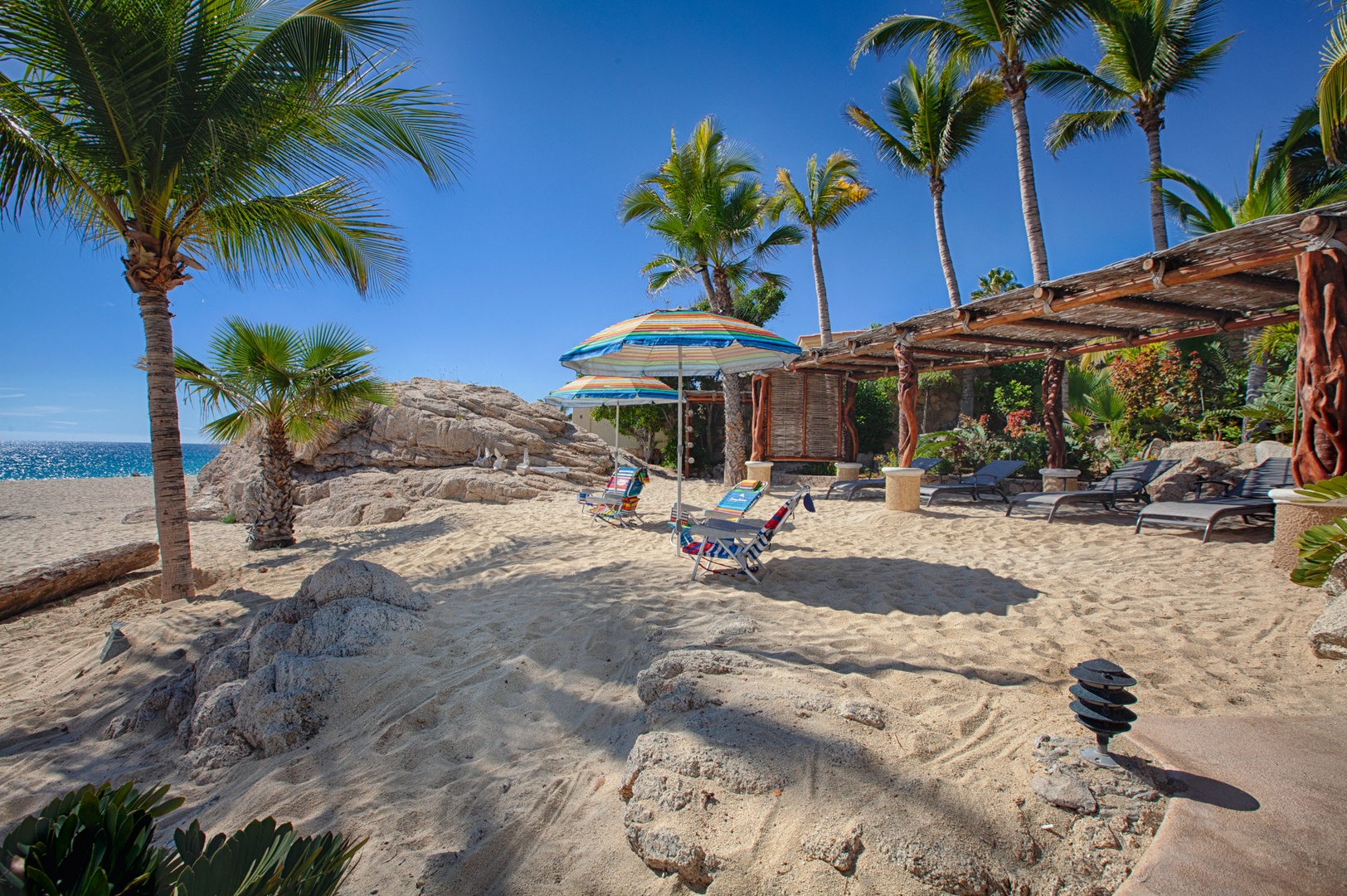 Private beachfront paradise with swaying palms, rocky formations, and rustic pergola creating the perfect tropical escape.