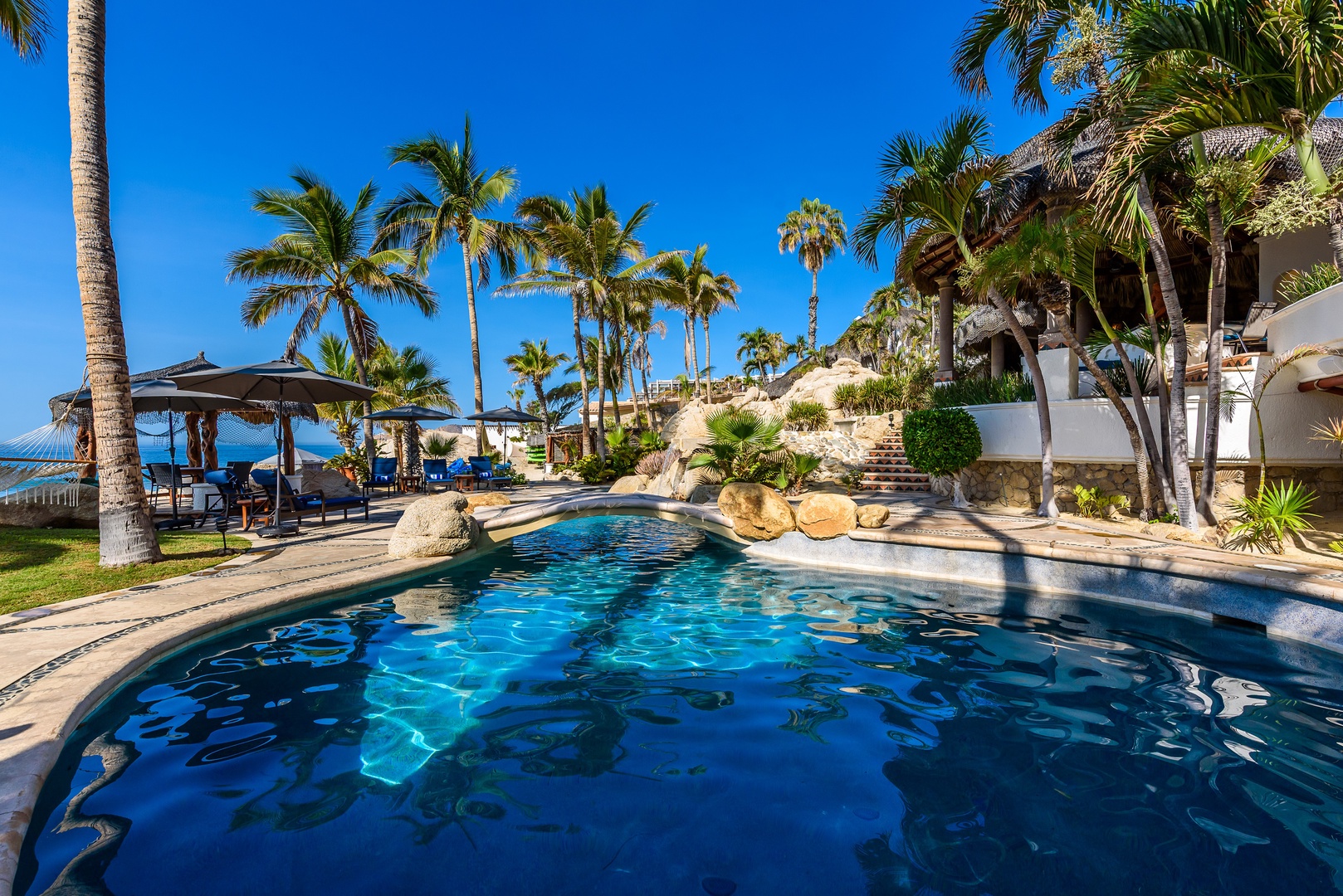 A sparkling infinity pool surrounded by tropical palms and native landscaping beckons you to unwind, with easy access to beachside lounging areas just steps away.