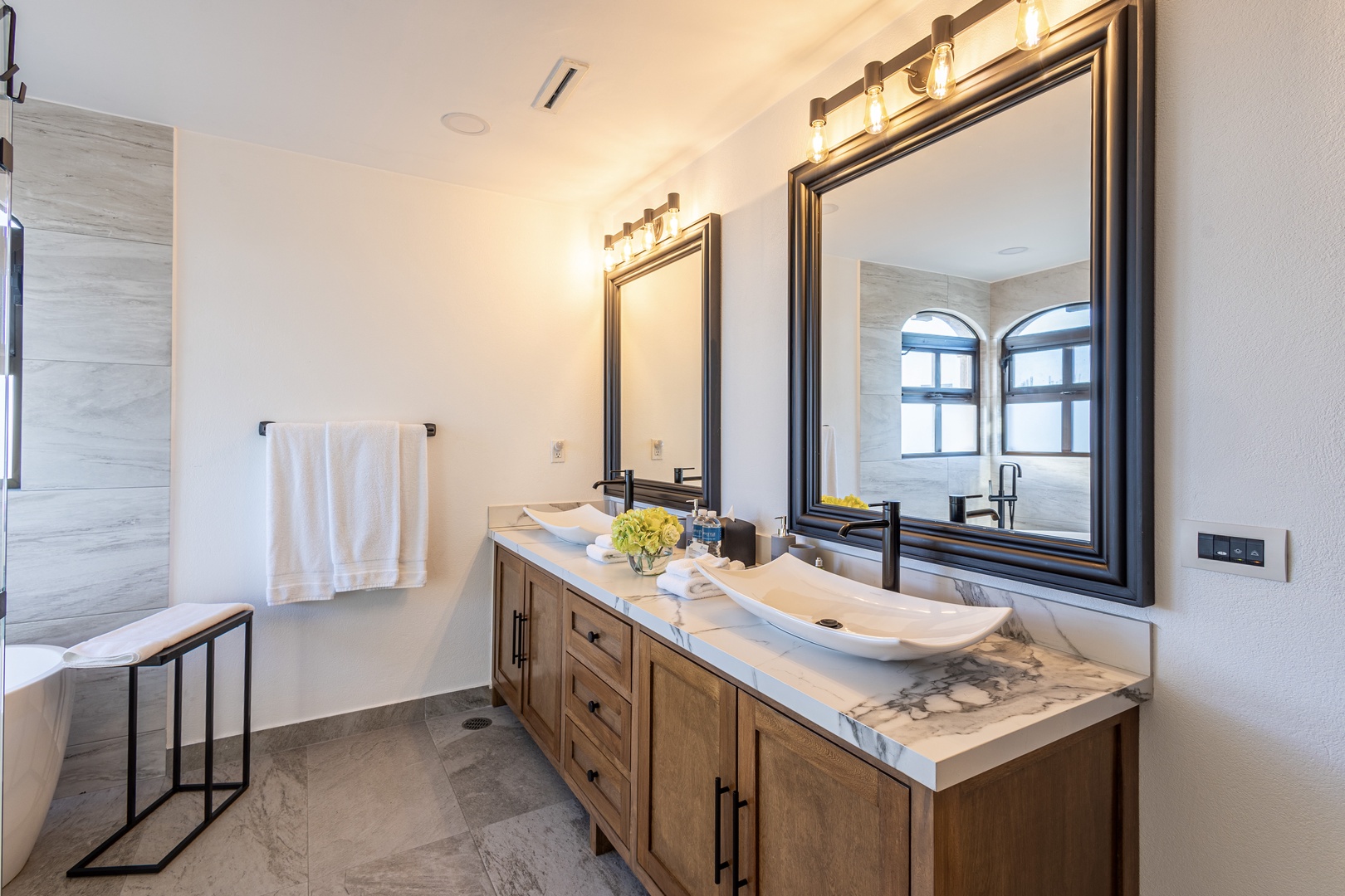 Step into your private sanctuary with elegant marble countertops, warm wood vanity, and designer fixtures. Fresh towels await your arrival, and natural light from arched windows brightens your morning routine beautifully.
