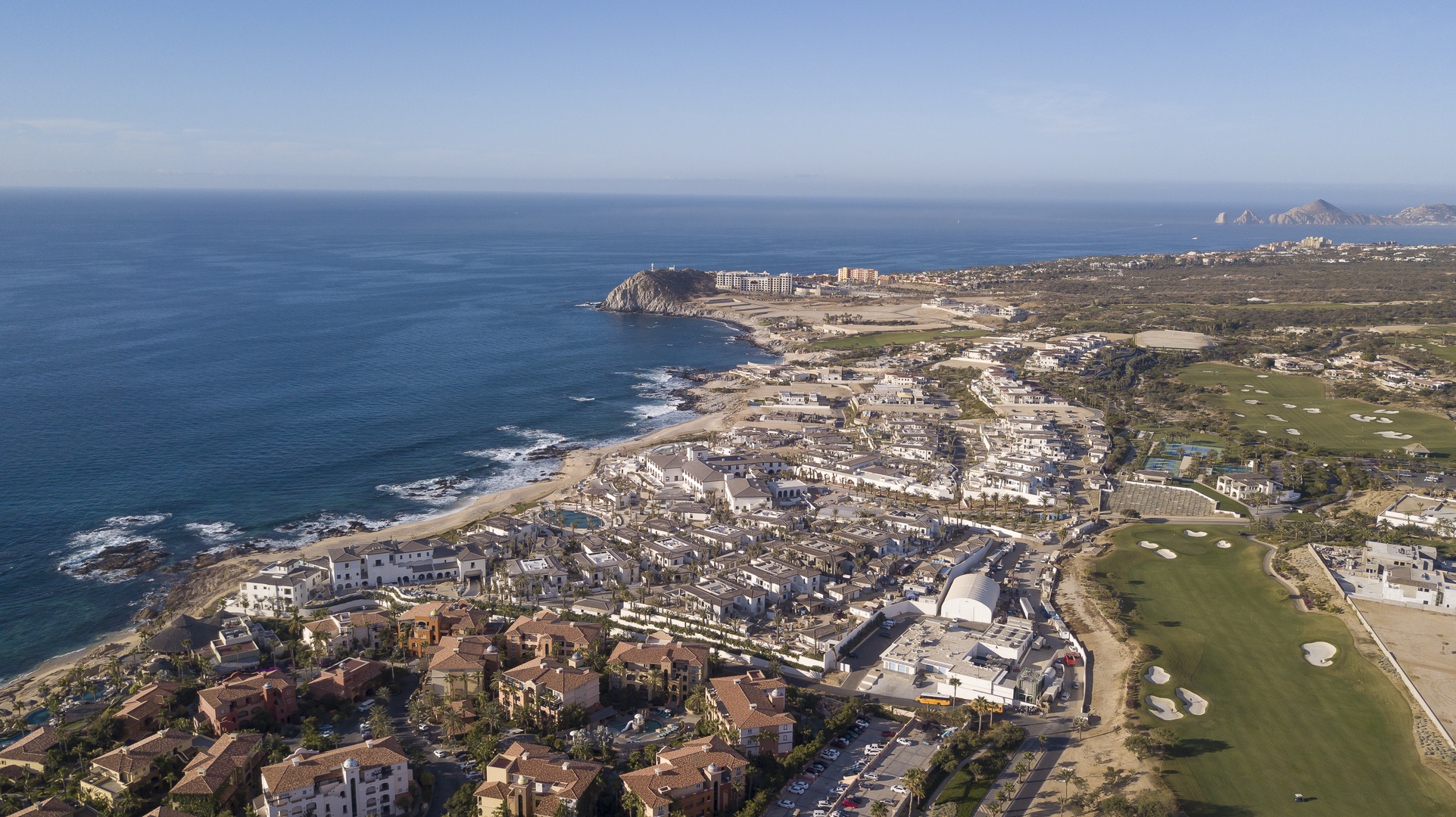 Aerial view of coastal resort community featuring oceanfront hotels, residential areas, and championship golf course along pristine Pacific coastline.