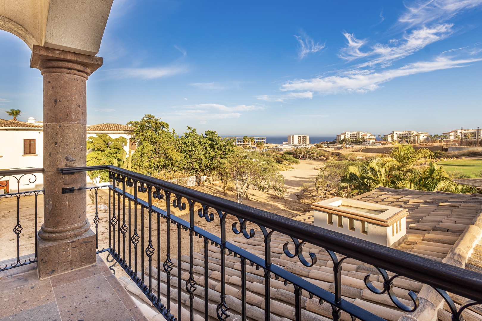 Sweeping views stretch across lush greens and natural landscape toward the sparkling sea, framed by elegant Mediterranean-style architecture with charming wrought-iron details.