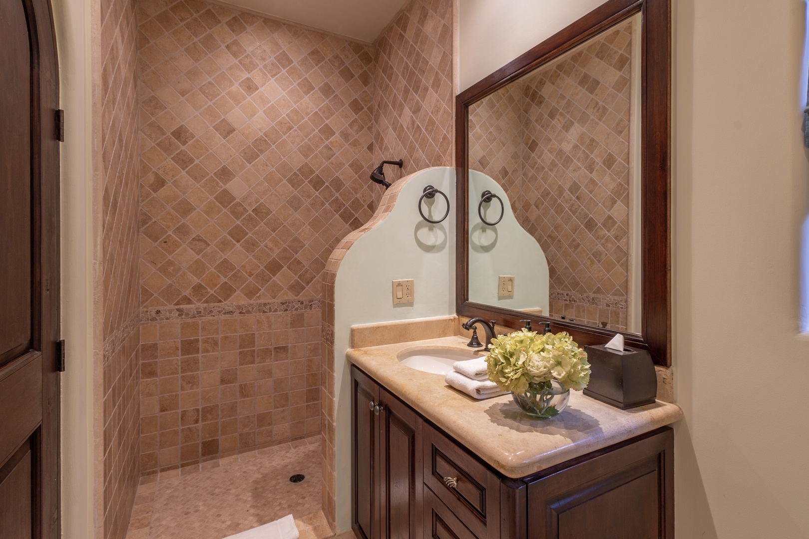 Step into your private bathroom with a custom tiled walk-in shower. Soft towels wait beside fresh blooms on the elegant vanity, ready for your stay.