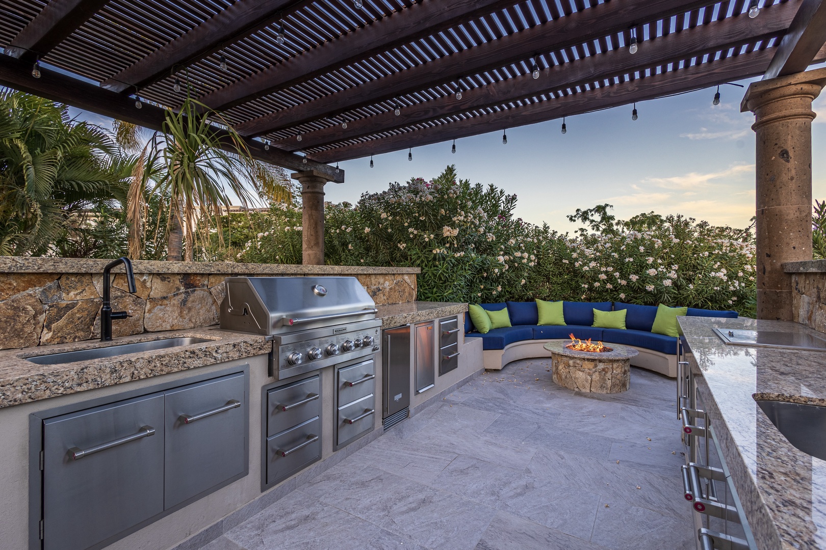 Gather around your private outdoor kitchen featuring a premium BBQ setup, stylish curved seating with a fire pit, and lush tropical views—perfect for evening entertaining under the stars.