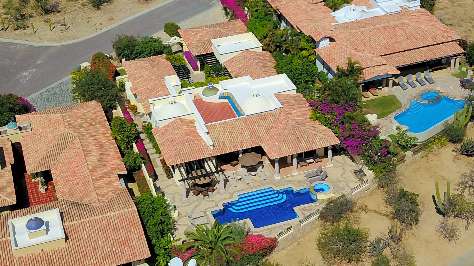 Aerial view of the expansive villa complex featuring multiple buildings with distinctive red tile roofing and private swimming pools set in desert landscape.