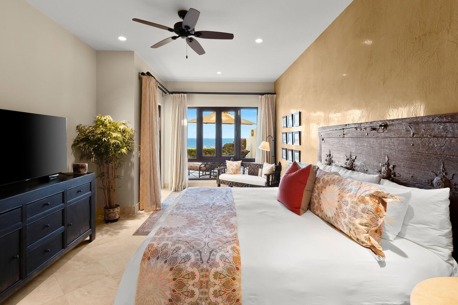 Wake up to breathtaking ocean views from your luxurious bedroom, where a rustic headboard and elegant bedding create a serene coastal retreat. Step through French doors to your private terrace and soak in the sea breeze.