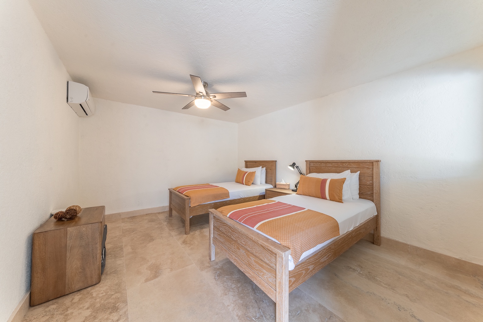 Your bright, breezy bedroom features two comfortable twin beds with crisp linens and warm sunset-toned accents. A ceiling fan and air conditioning keep the space cool and relaxing after your day's adventures.