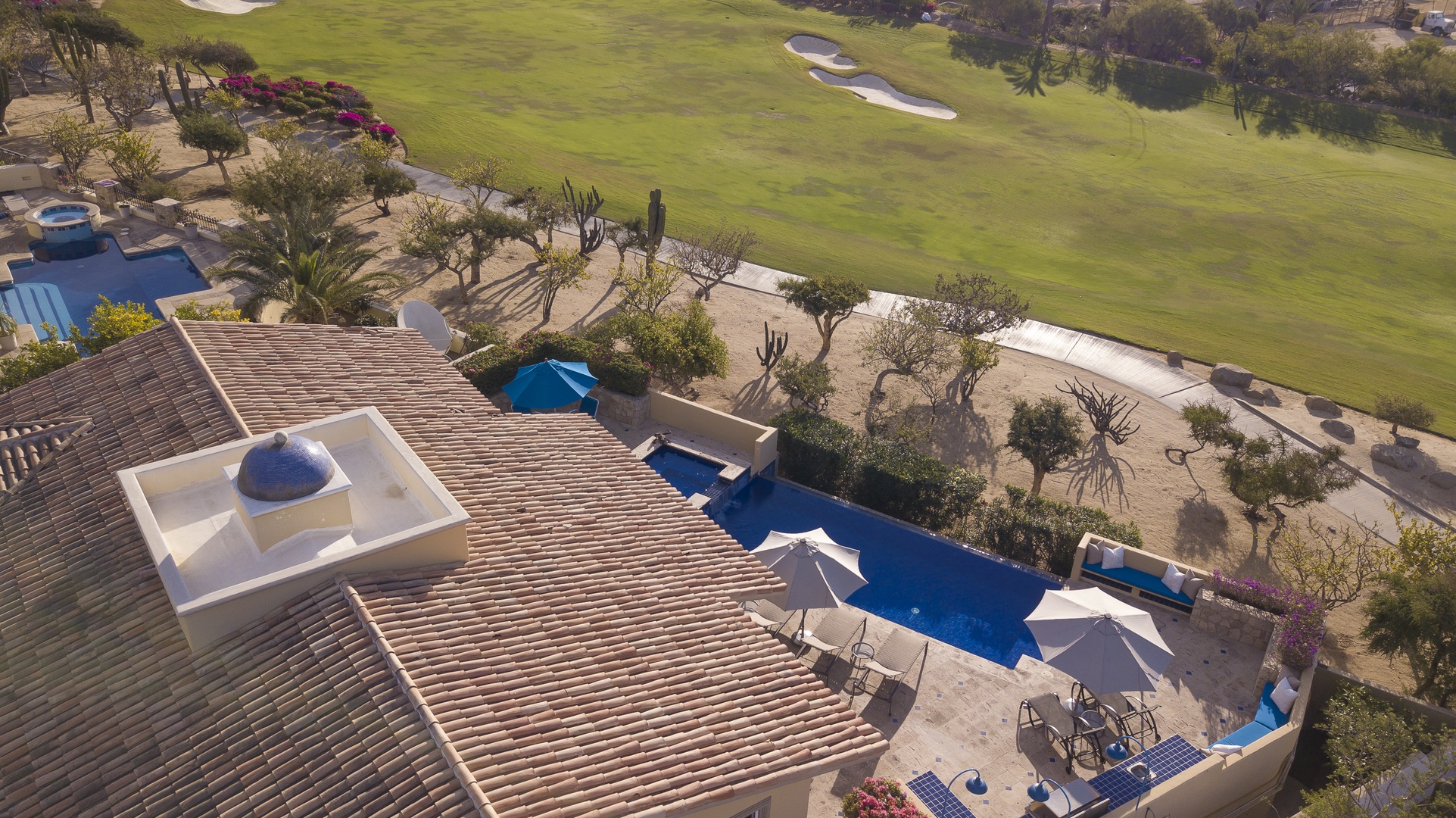 Aerial view of luxury villa featuring private pool and hot tub, nestled beside pristine golf course fairways in desert landscape.