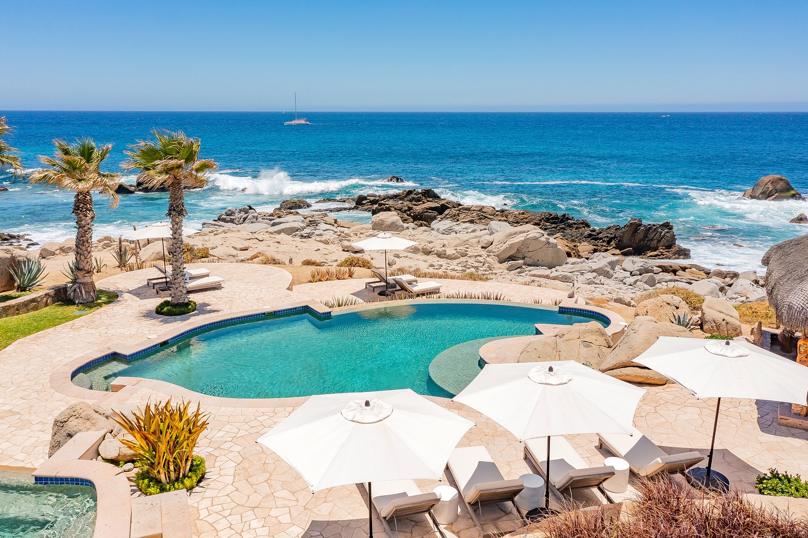 Stunning oceanfront pool area with pristine sea views, rocky coastline, and tropical palm trees creating the perfect coastal retreat.