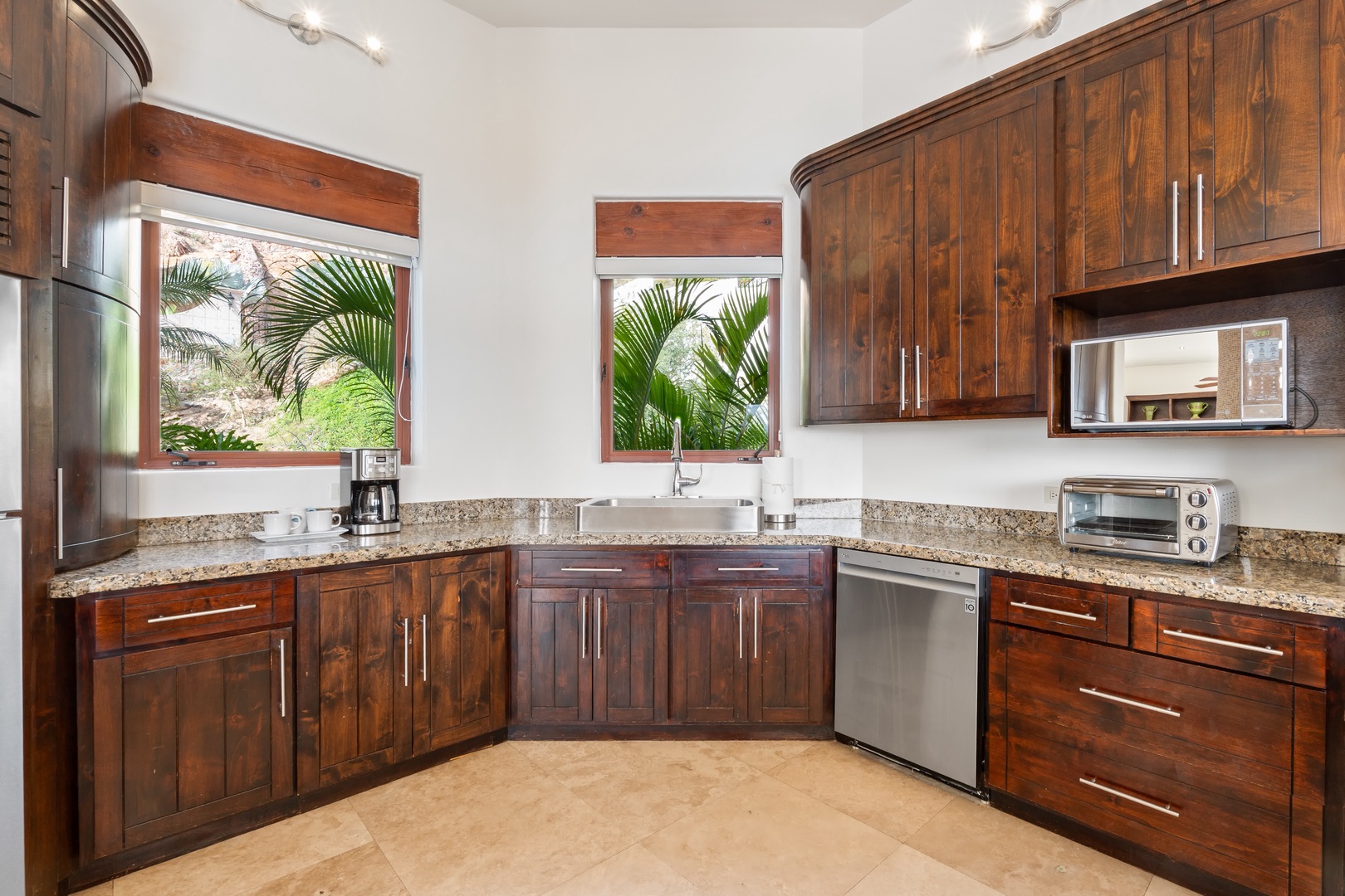 Your fully equipped kitchen features rich wood cabinets, granite countertops, and tropical garden views through charming windows.