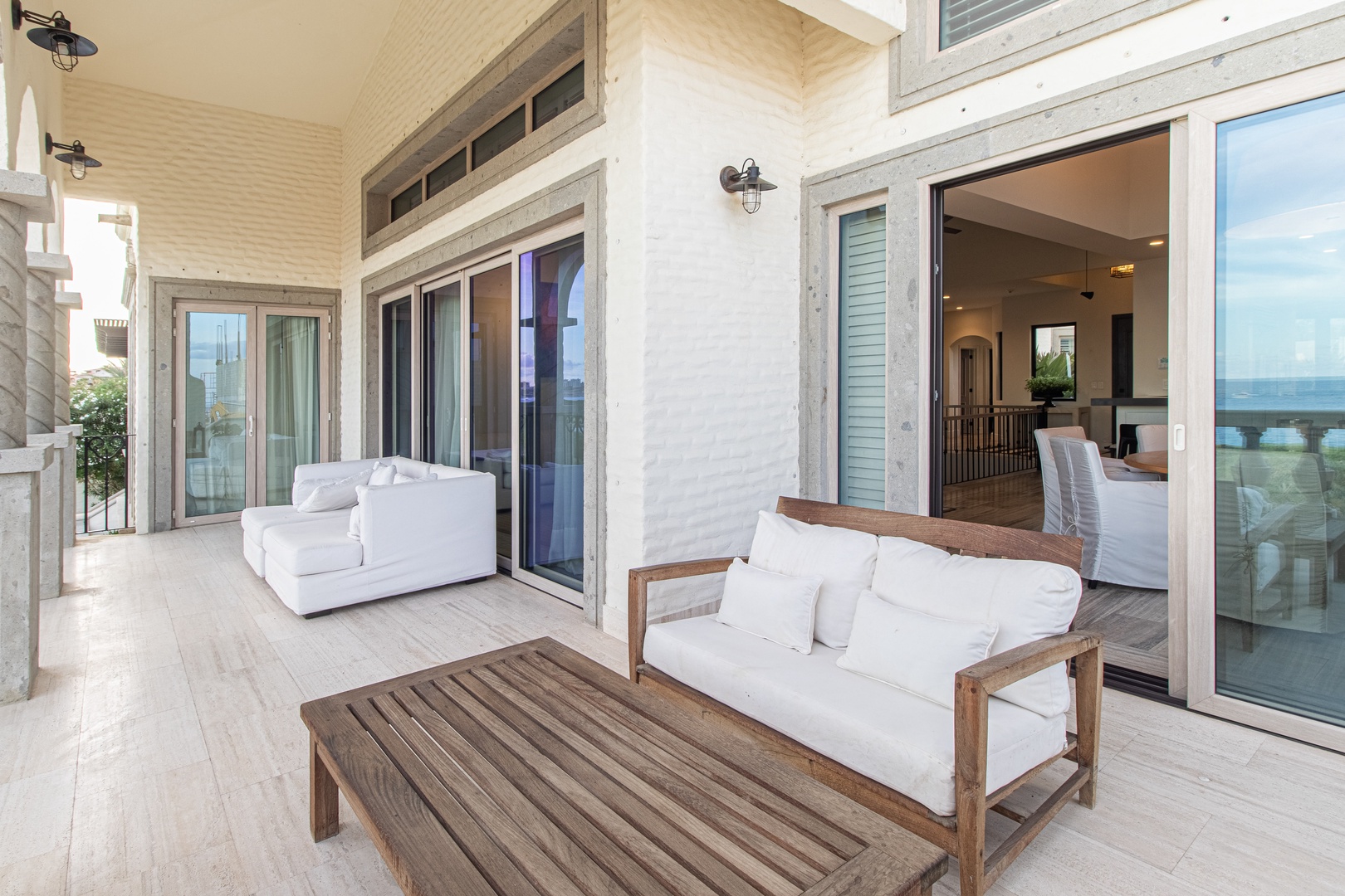 Step onto your private covered terrace with plush seating overlooking the water. Natural light pours through tall glass doors, while white shutters add coastal charm to this seamless indoor-outdoor retreat.