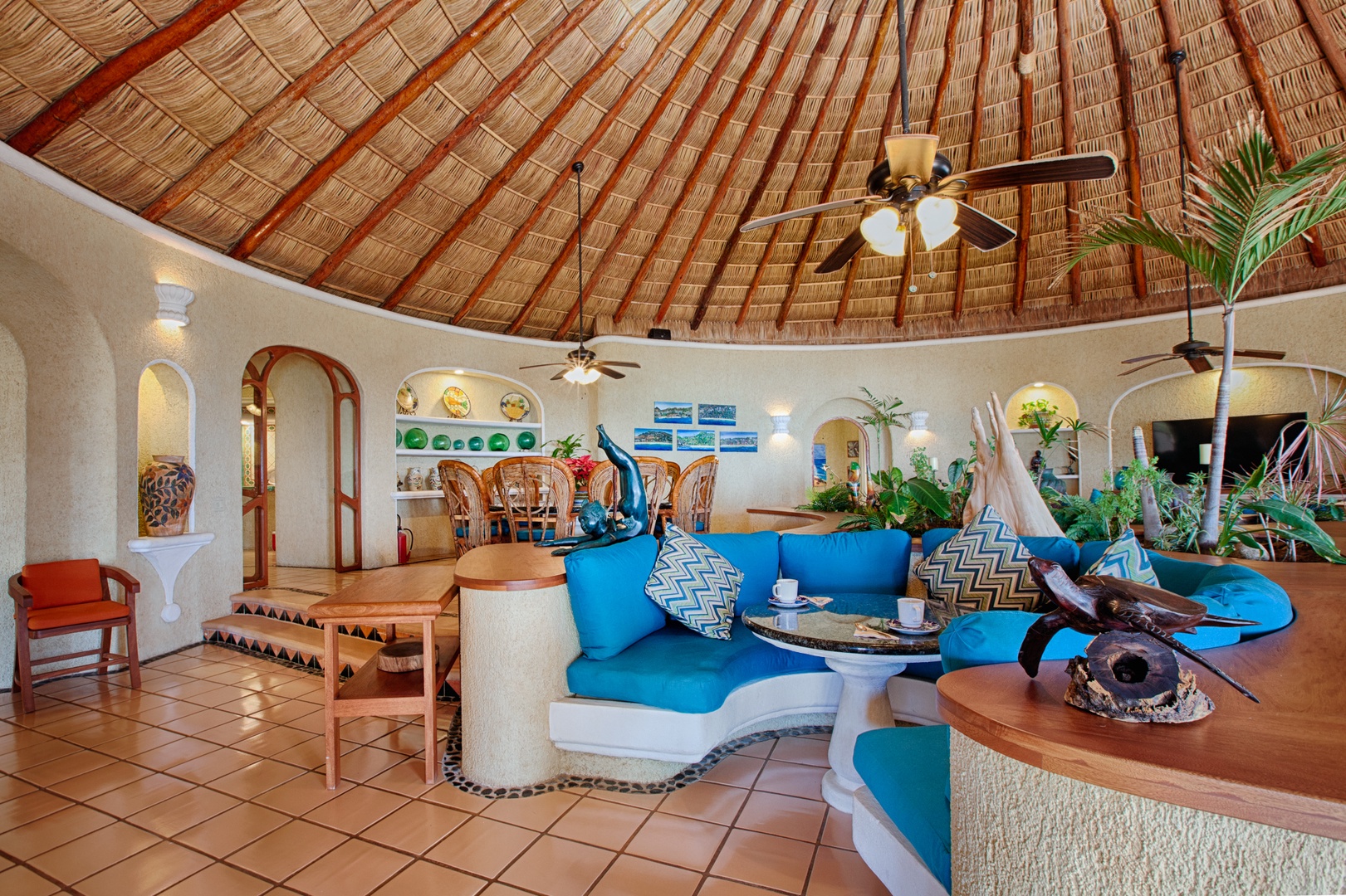 Relax in your stunning palapa-style living room with soaring thatched ceilings, vibrant blue seating, and tropical charm throughout.