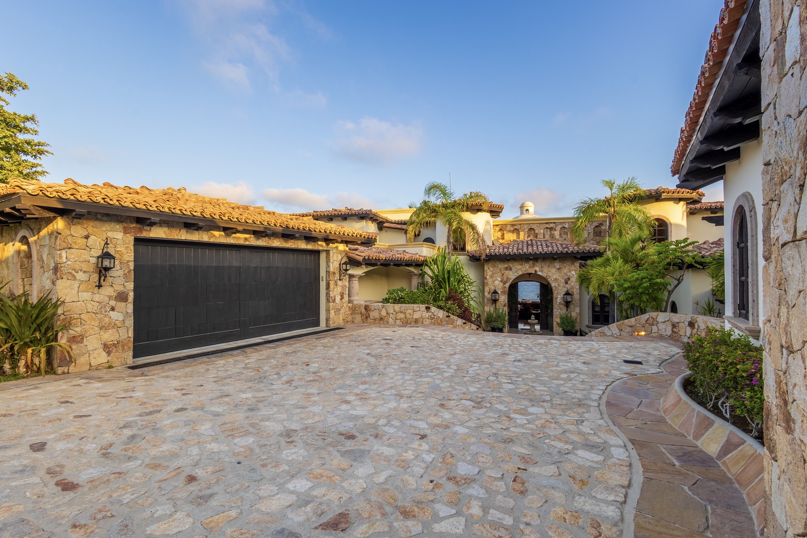 This stunning Mediterranean-style entrance welcomes you with terracotta-tiled roofs, rustic stonework, and lush tropical landscaping—a beautiful arrival setting for your vacation.