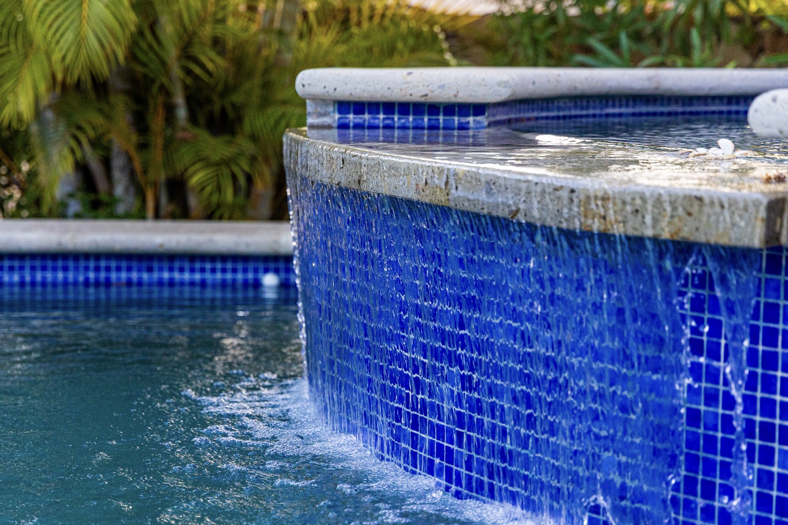 A sparkling blue-tiled pool with gentle waterfall features creates a serene oasis surrounded by lush tropical greenery—your private retreat for relaxation.