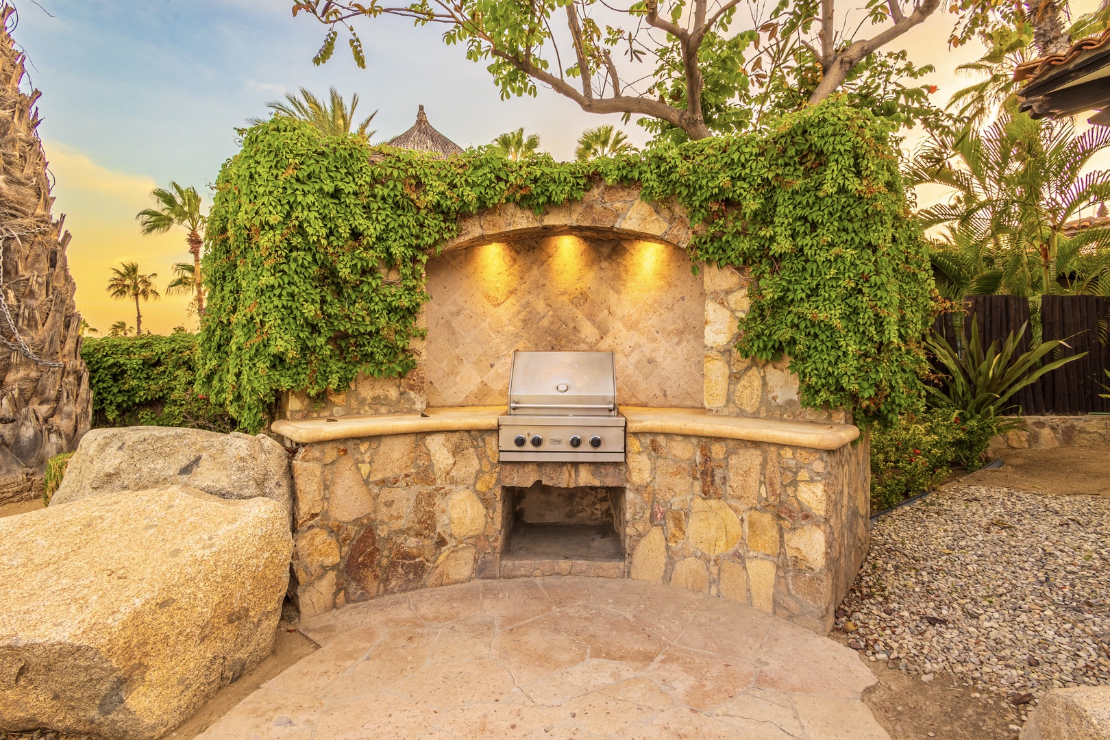 Step into your own outdoor paradise with this stunning grill station framed by lush greenery and ambient lighting, perfect for memorable sunset cookouts.