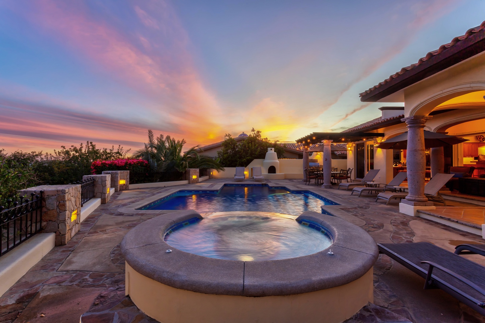Stunning sunset paints the sky in vibrant hues over this luxurious villa's pool deck and hot tub area.