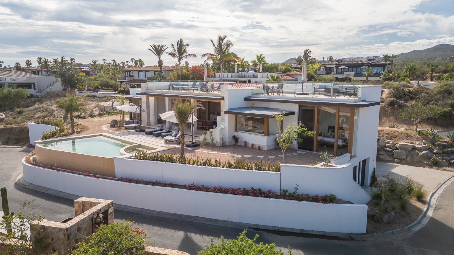 Stunning contemporary villa set within a resort community, showcasing multiple levels, rooftop terraces, and tropical landscaping beneath a wide desert sky.