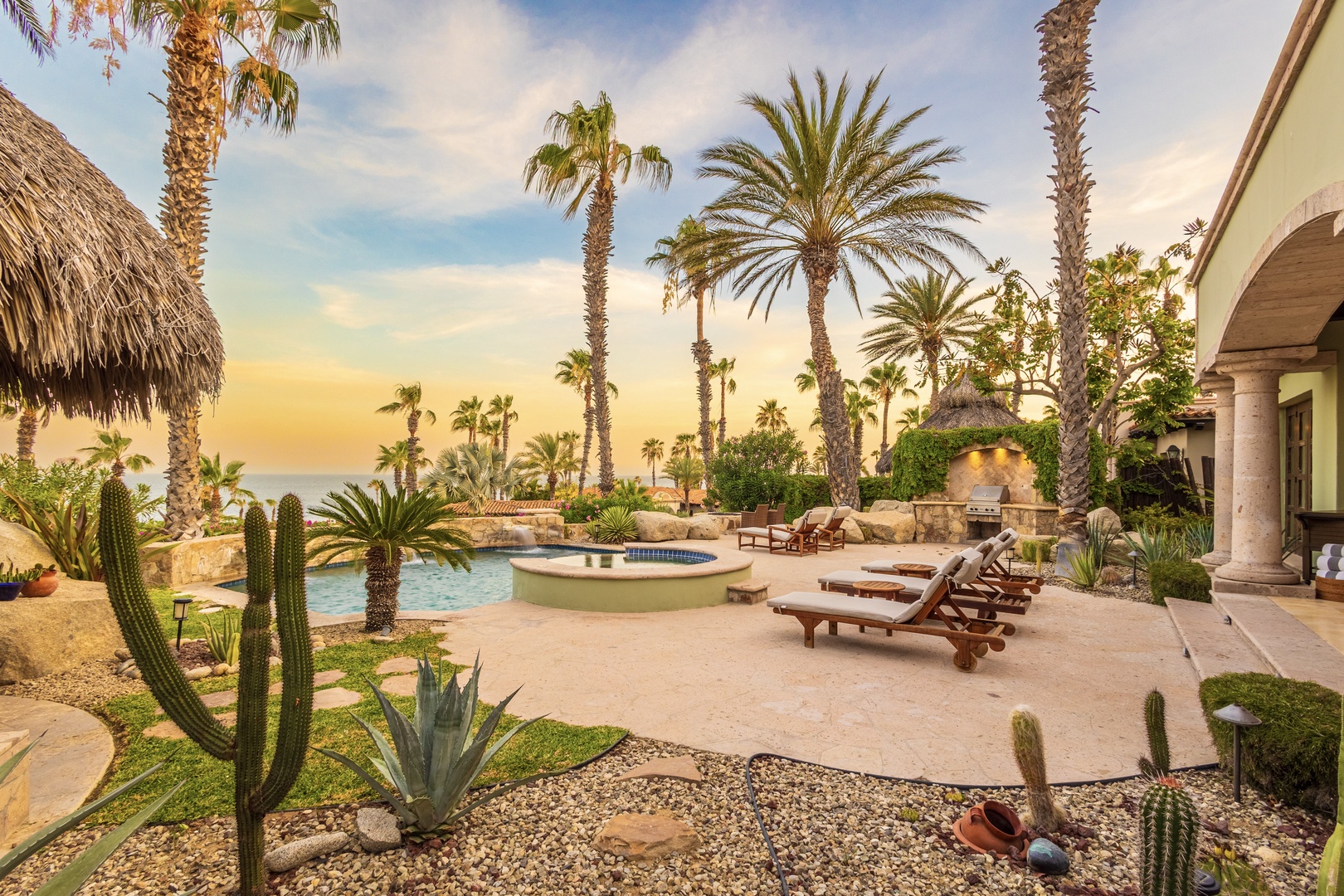 Tropical paradise with ocean views, private pool, hot tub, and sun-soaked loungers nestled among towering palms and desert succulents in a tranquil beachfront setting.