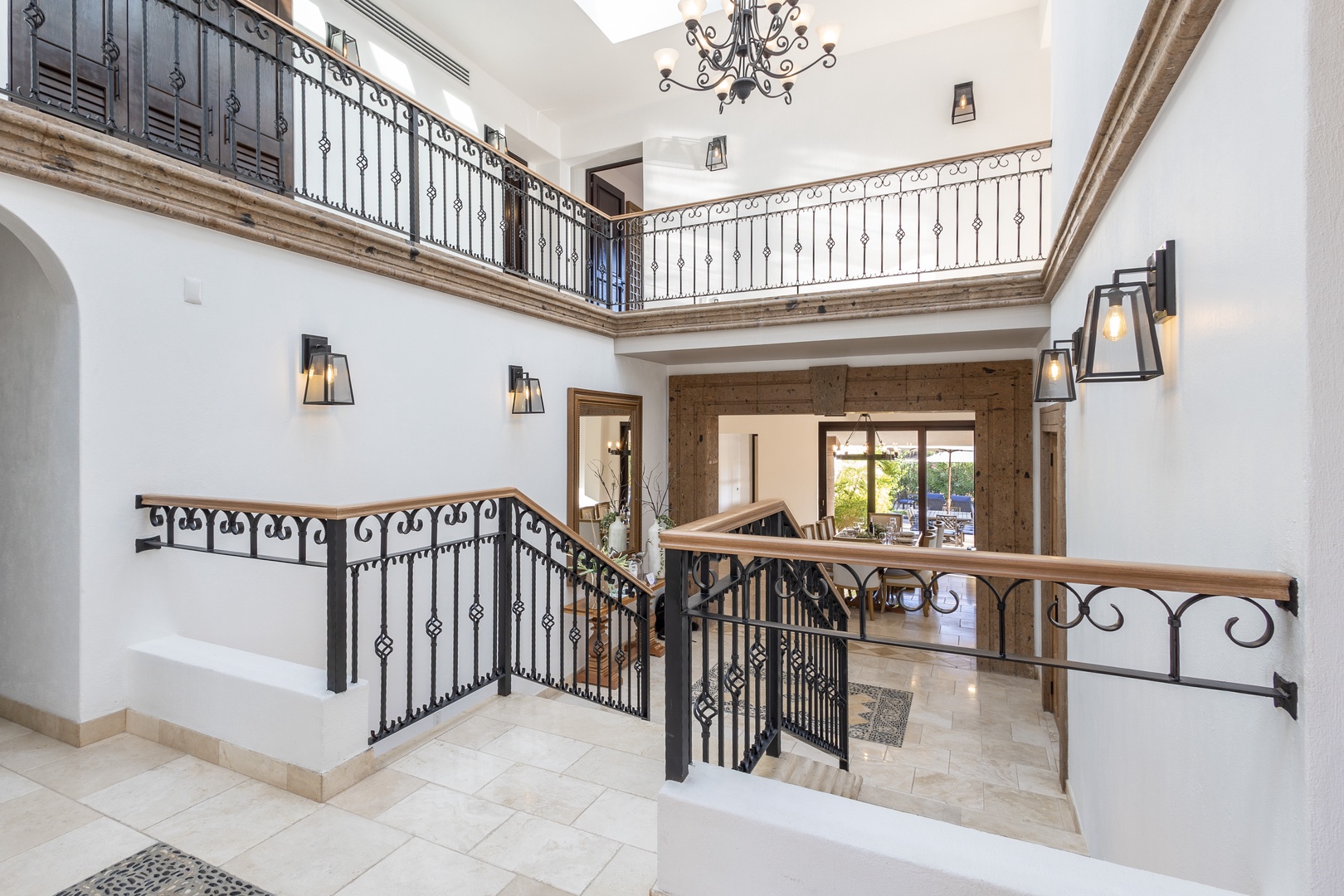 A stunning two-story entrance hall welcomes guests with soaring ceilings, elegant wrought-iron railings, and warm lighting that creates an inviting, luxurious atmosphere from the moment you arrive.