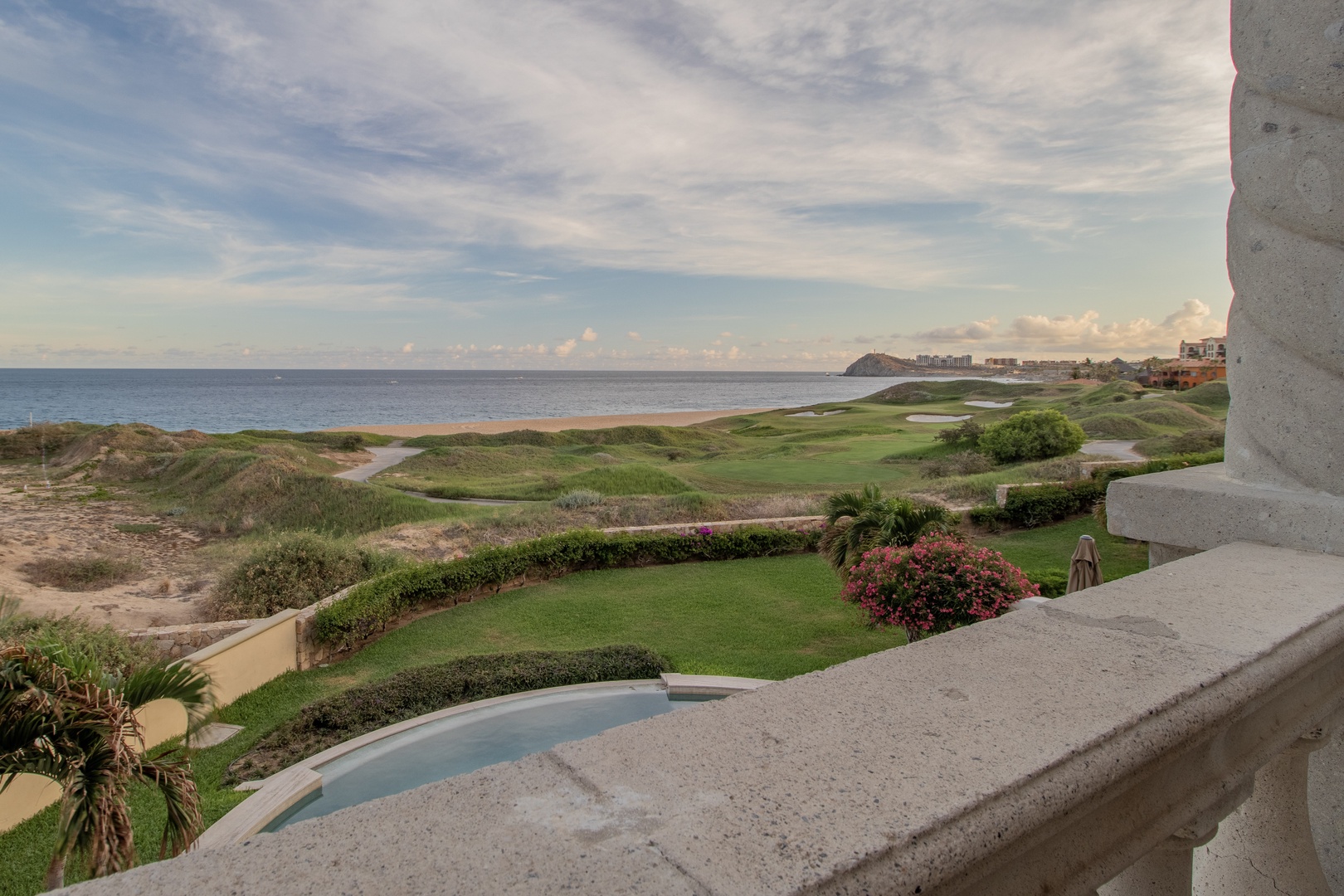 Oceanfront property featuring lush golf course fairways, manicured lawns, and sweeping coastal views stretching toward distant shoreline development under expansive skies.