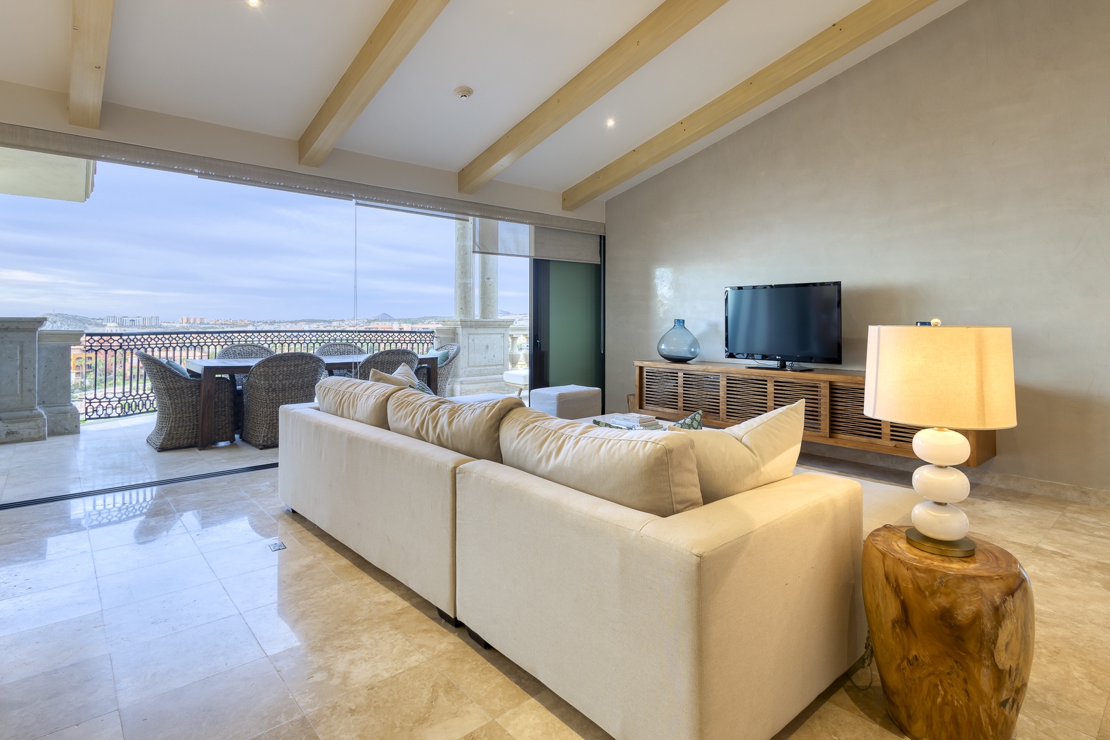 Unwind in your bright, open living space featuring vaulted ceilings with elegant exposed beams, plush seating, and seamless access to your private terrace overlooking the city skyline.