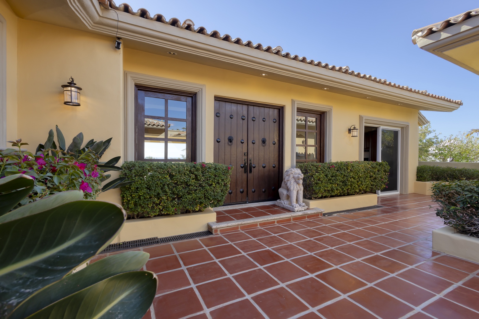 Mediterranean-style entrance features warm yellow walls, decorative stonework, and welcoming tile flooring surrounded by lush landscaping.