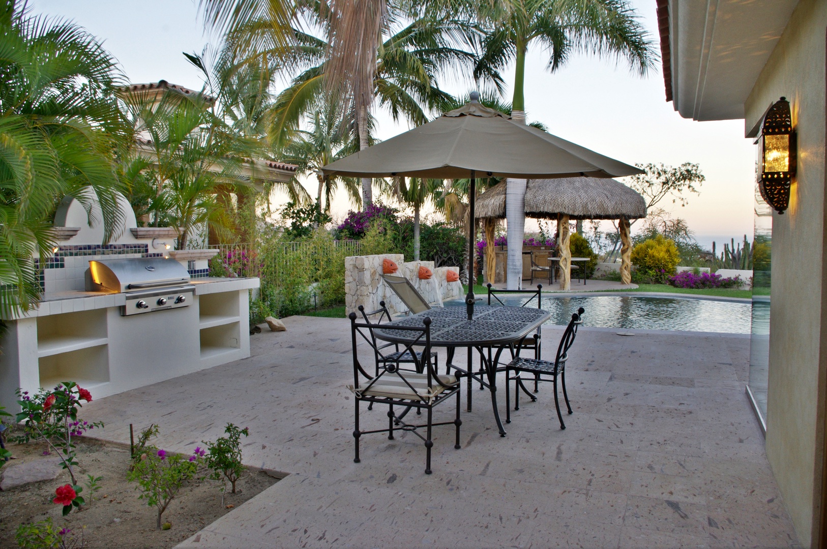 Your private outdoor oasis awaits with alfresco dining, a built-in BBQ kitchen, and a sparkling pool surrounded by tropical palms and colorful blooms—perfect for sunset gatherings.