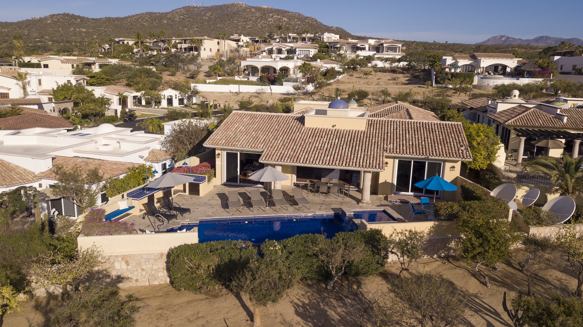 Stunning aerial view of a luxury villa with private pool nestled in the hills, surrounded by mountain landscape and neighboring properties.