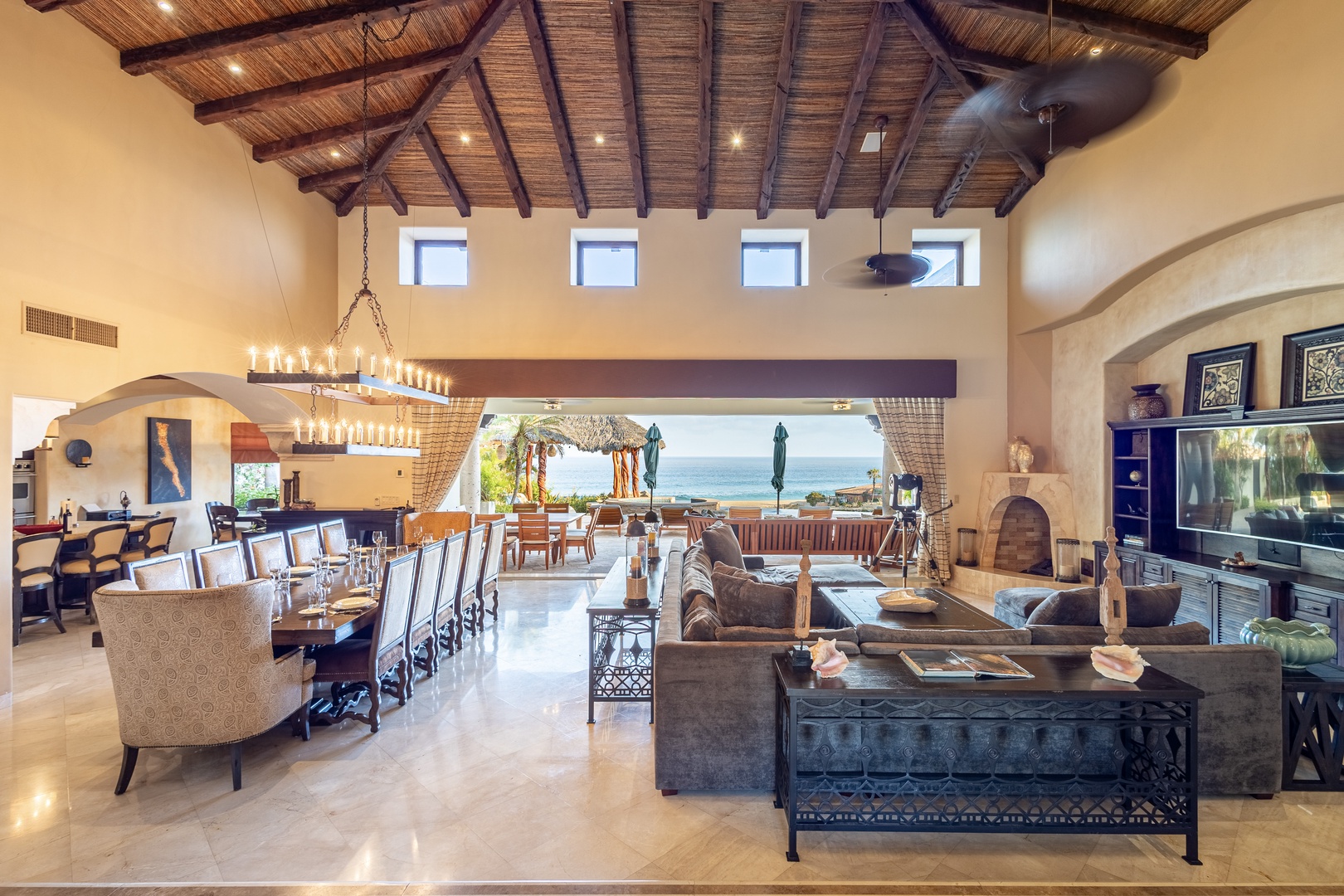 Unwind in your spacious living and dining area, where soaring wood-beamed ceilings and grand chandeliers frame sweeping ocean views through the open wall, perfect for relaxed gatherings and memorable meals.